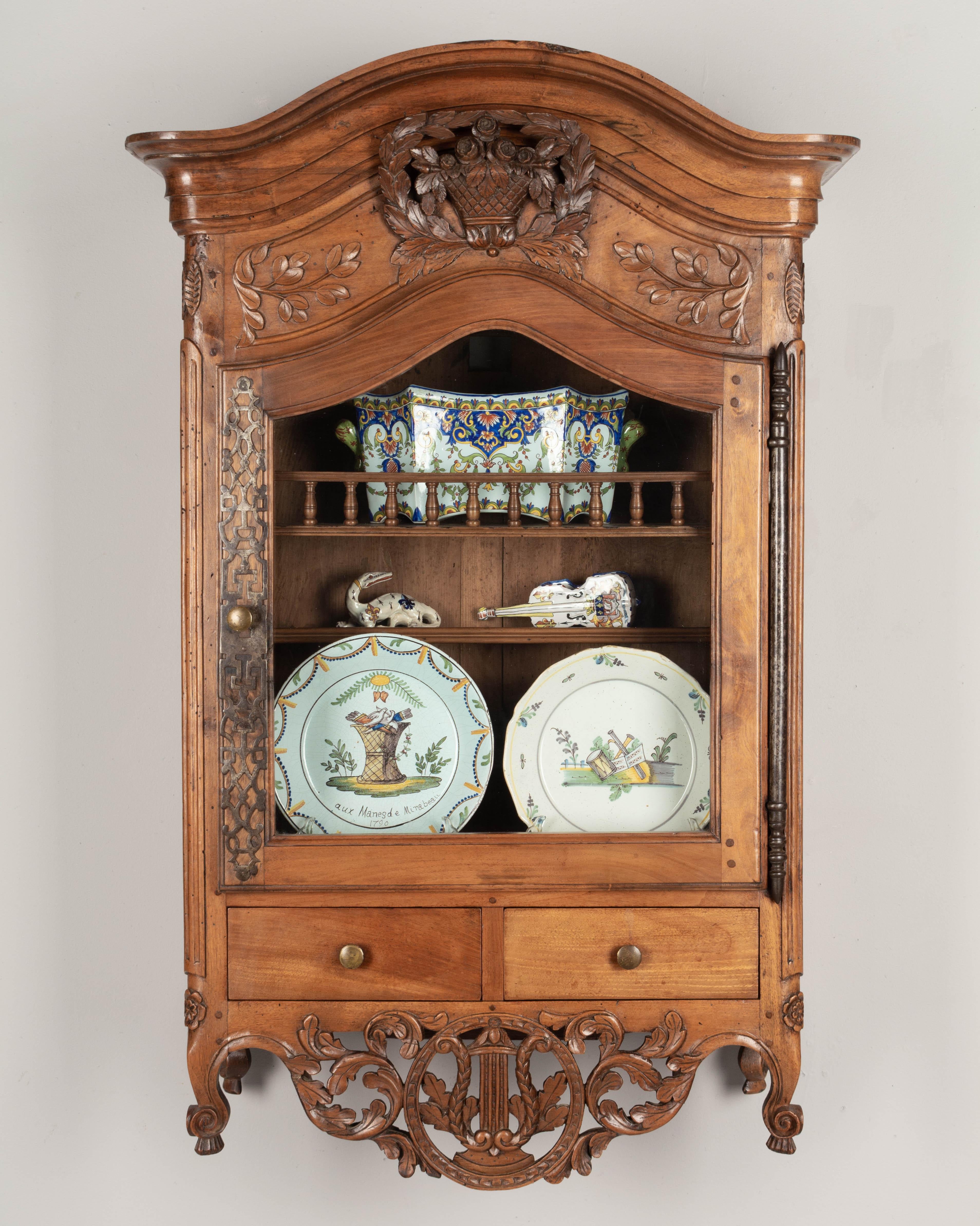 A late 18th century Louis XV style French Provençal verrio, or wall display cabinet from Nîmes. Made of solid walnut with beautifully carved details including a three dimensional basket of roses framed by a laurel wreath and a pierced apron with an