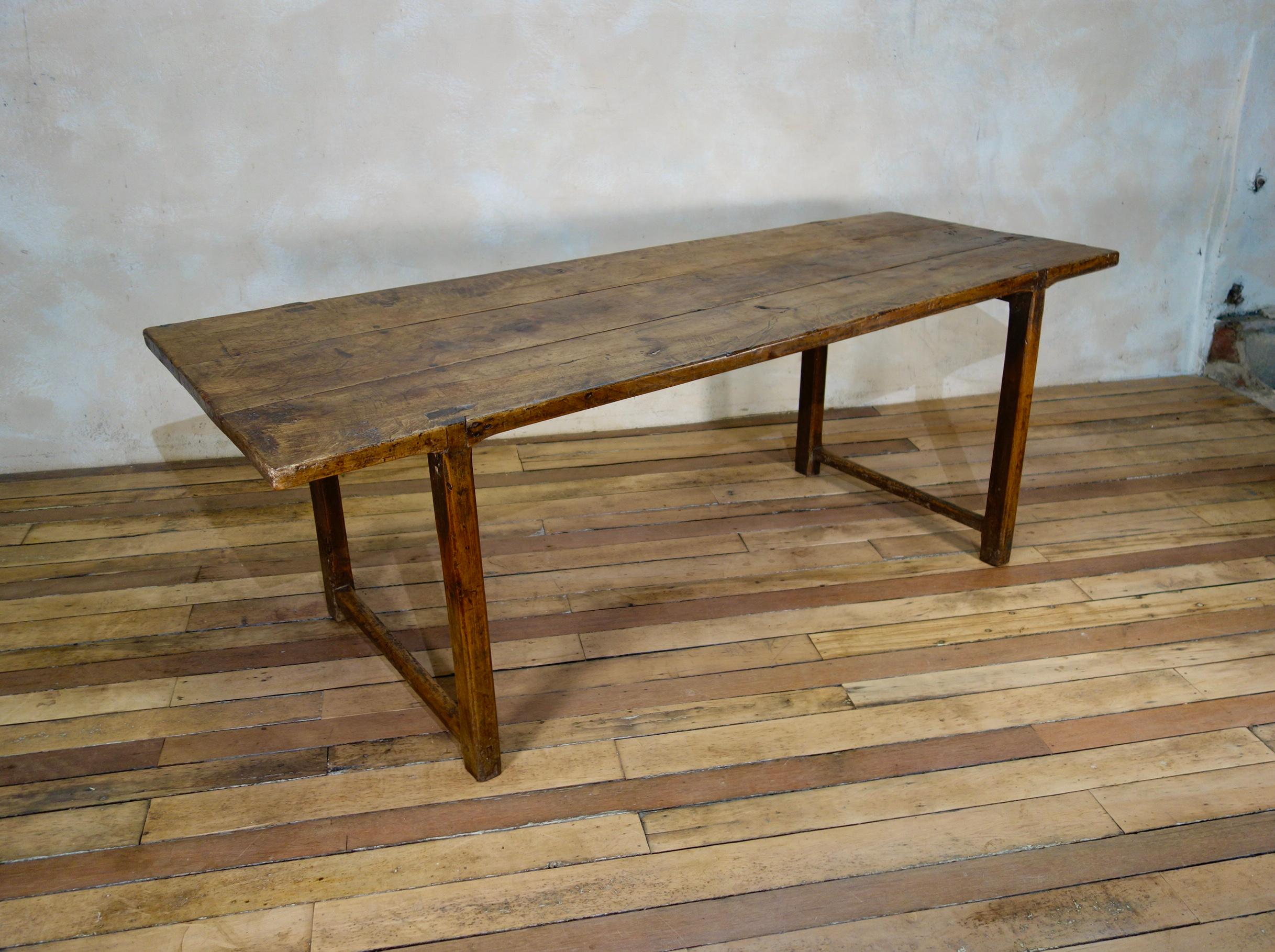 An elegant early 18th century French provincial cherry wood farmhouse table. Demonstrating a simplistic design with charming joints visible through the top of the table. Featuring a thick three plank top raised on chamfered legs with refectory