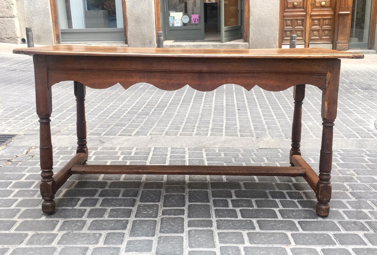 Rustic French oak table with turned legs and crossed stretcher from the 18th century. This table has a rectangular top with rounded corners that sit on an apron. The base is four turned legs. The legs are connected to each other with a crossed