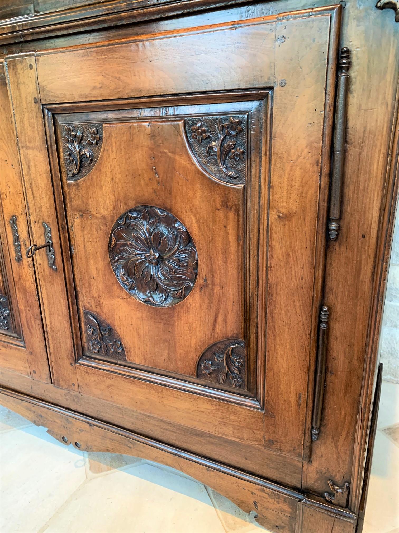 Very fine 18th century French red walnut cabinet or armoire with a rich honey-colored patina. The cupboard doors feature recessed foliate carvings accented by carved floral sprays at the corners. Retains the original handwrought iron hinges and