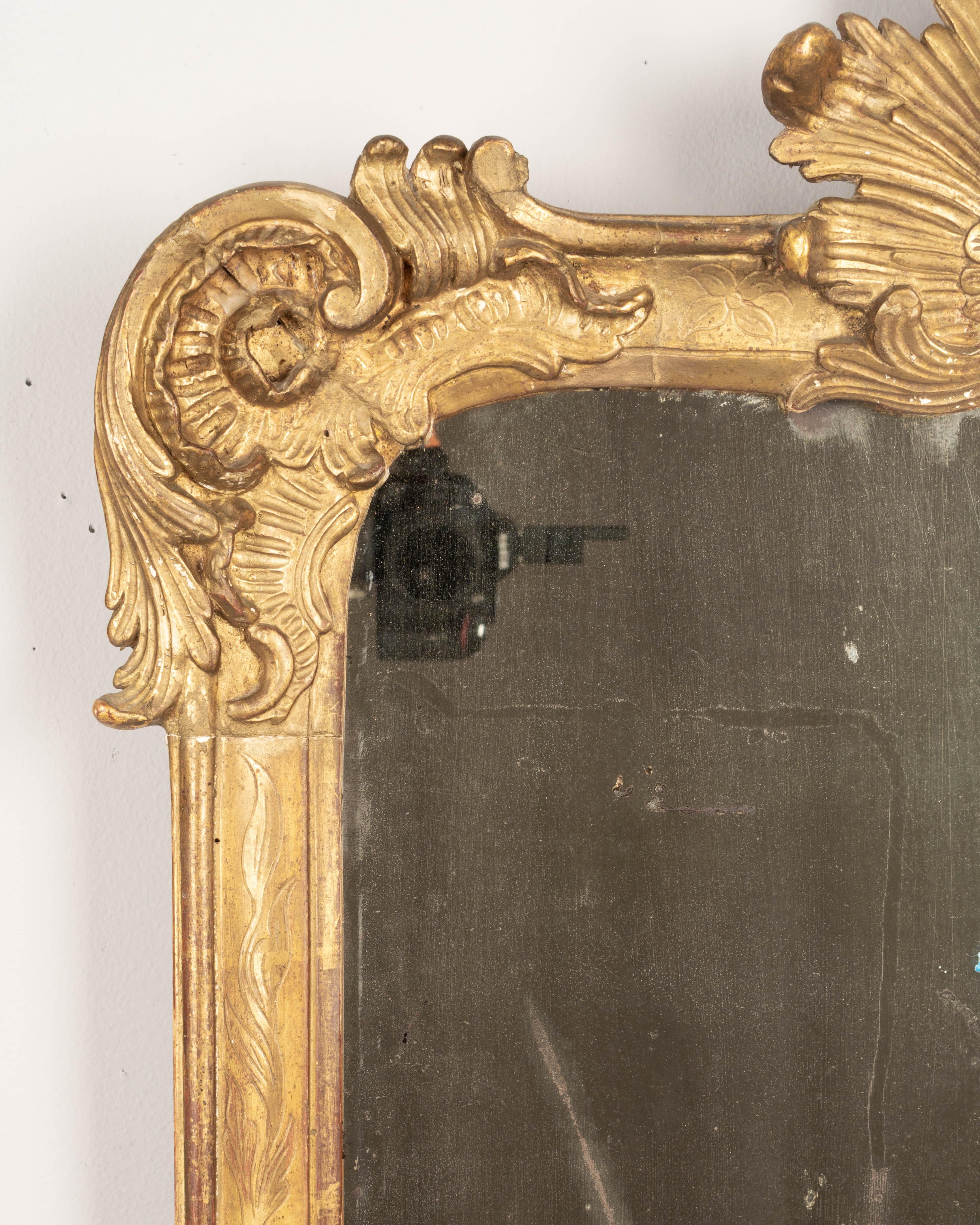 Miroir en bois doré de la période de la Régence, du XVIIIe siècle, avec une crête en forme de soleil et un décor d'angle incurvé en forme de volute. Belle patine avec une finition dorée pâle. Miroir d'origine avec de l'argenture ancienne et de