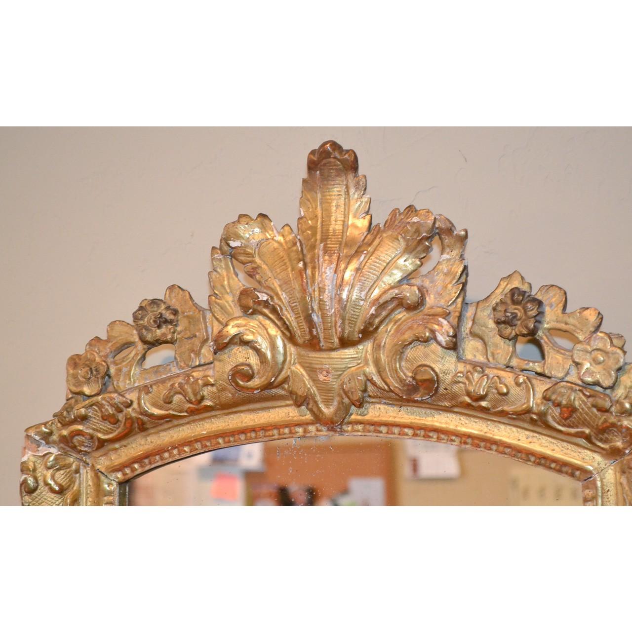 Finely carved late 18th century French Regence style giltwood wall or console mirror. The shaped crest features a large hand-carved leaf-spray and trailing flower vines. The border carved in the round and in relief with stylized foliate designs. The