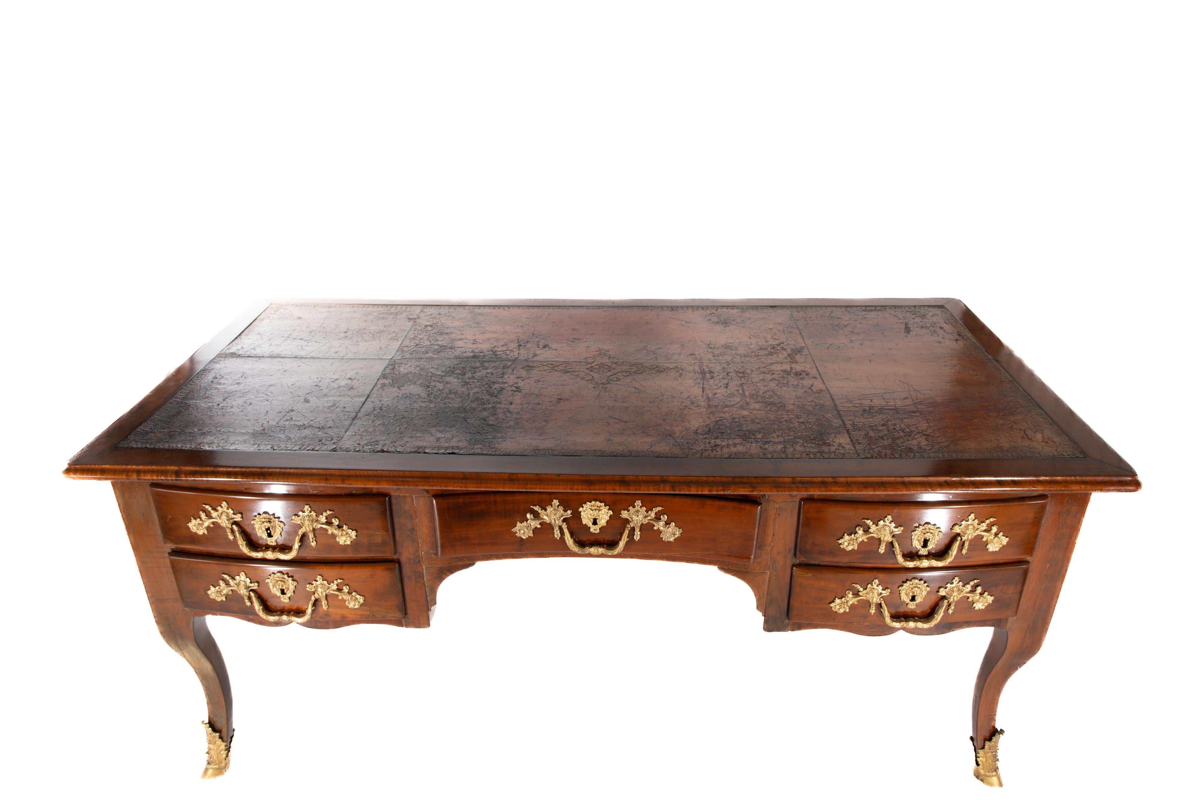 Beautiful 18th century French Regence Bureau Plat.  Four drawers, with pieced leather top with carved design in the center and around the edges.
Walnut wood with gilded hardware resting on gilded hoof feet.
Includes two keys and additional pull.