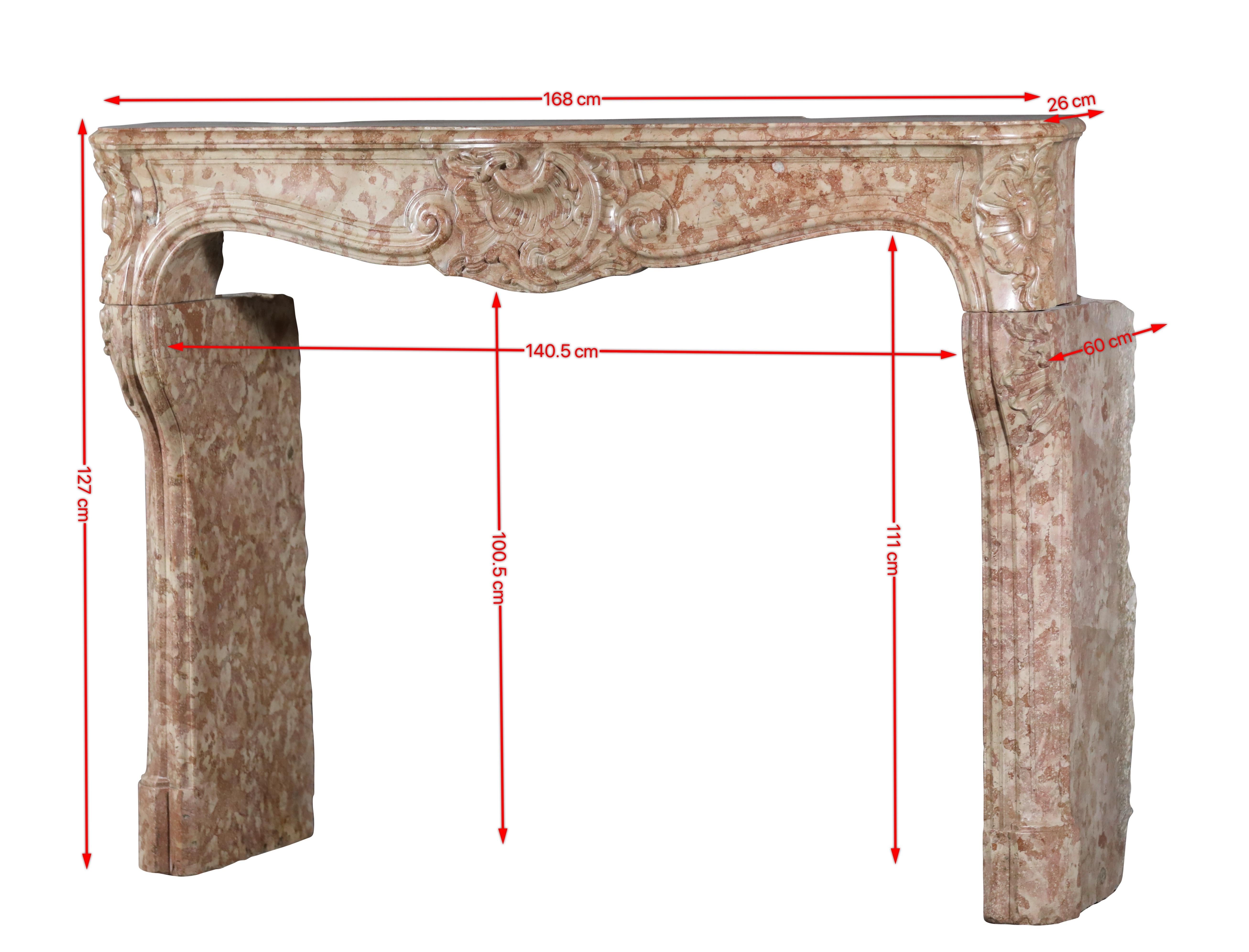 This authentic mid-18th century French Regency fireplace surround is a rare masterpiece in Rose de Bourgogne hard stone from the Burgundy region. Its warm pink-beige hues with natural veining, smooth surface, and refined Rococo carvings create a