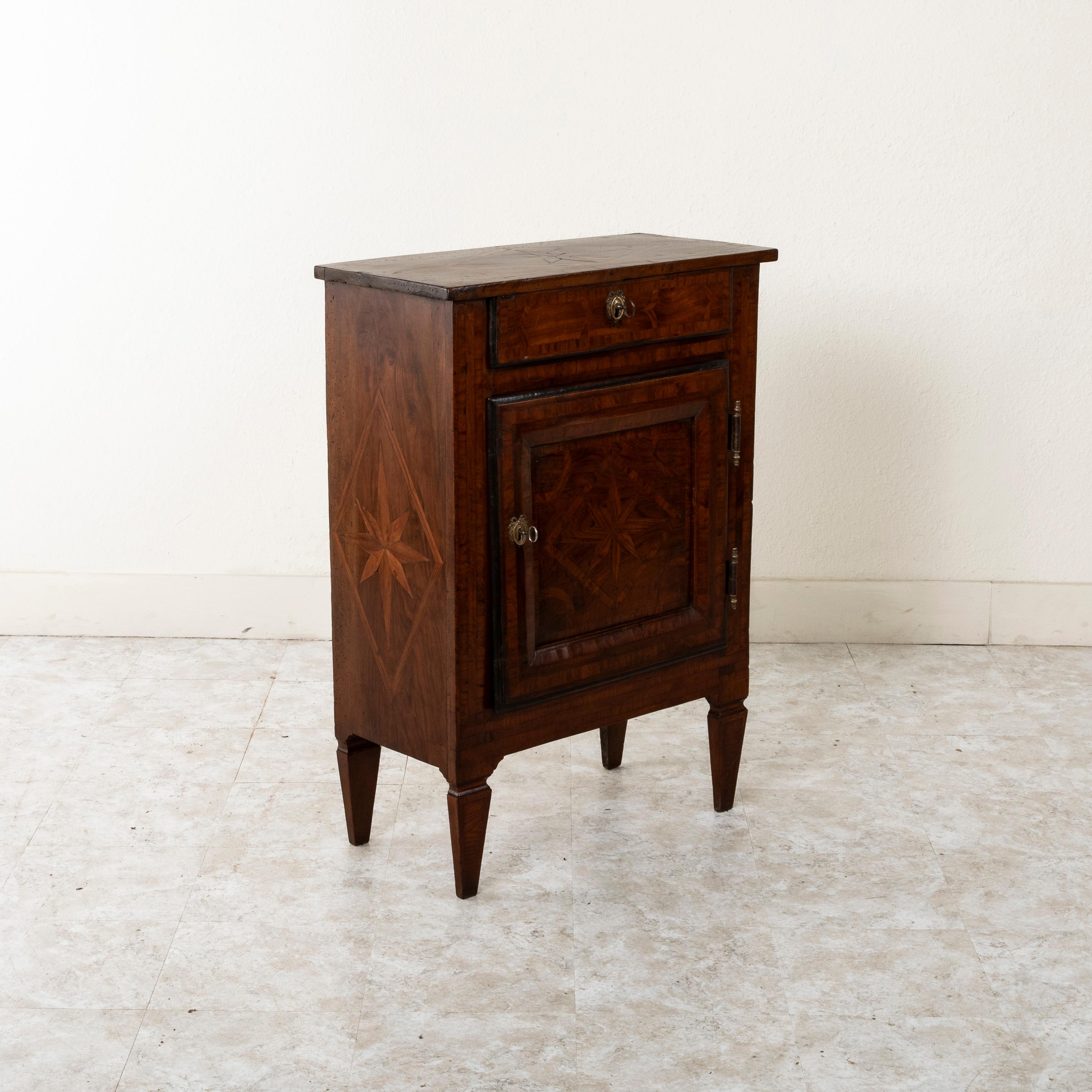 This late eighteenth century French Regency period walnut and rosewood marquetry cabinet or nightstand features geometric starburst patterns inset within diamond lozenges on the top, sides, and door. An upper drawer and its lower door are fitted