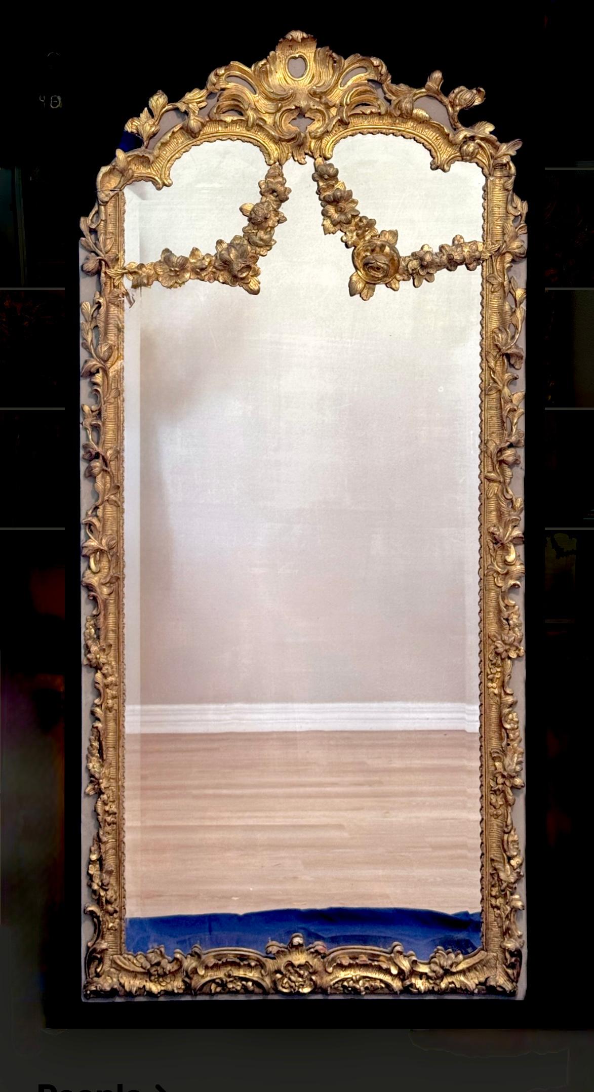 Regal 18th Century French Rococo Painted Giltwood Wall Mirror. Mirror is styled in the Rococo tradition, characterized by its ornate, asymmetrical decoration and naturalistic motifs. Mirror top features a large central cartouche that often
