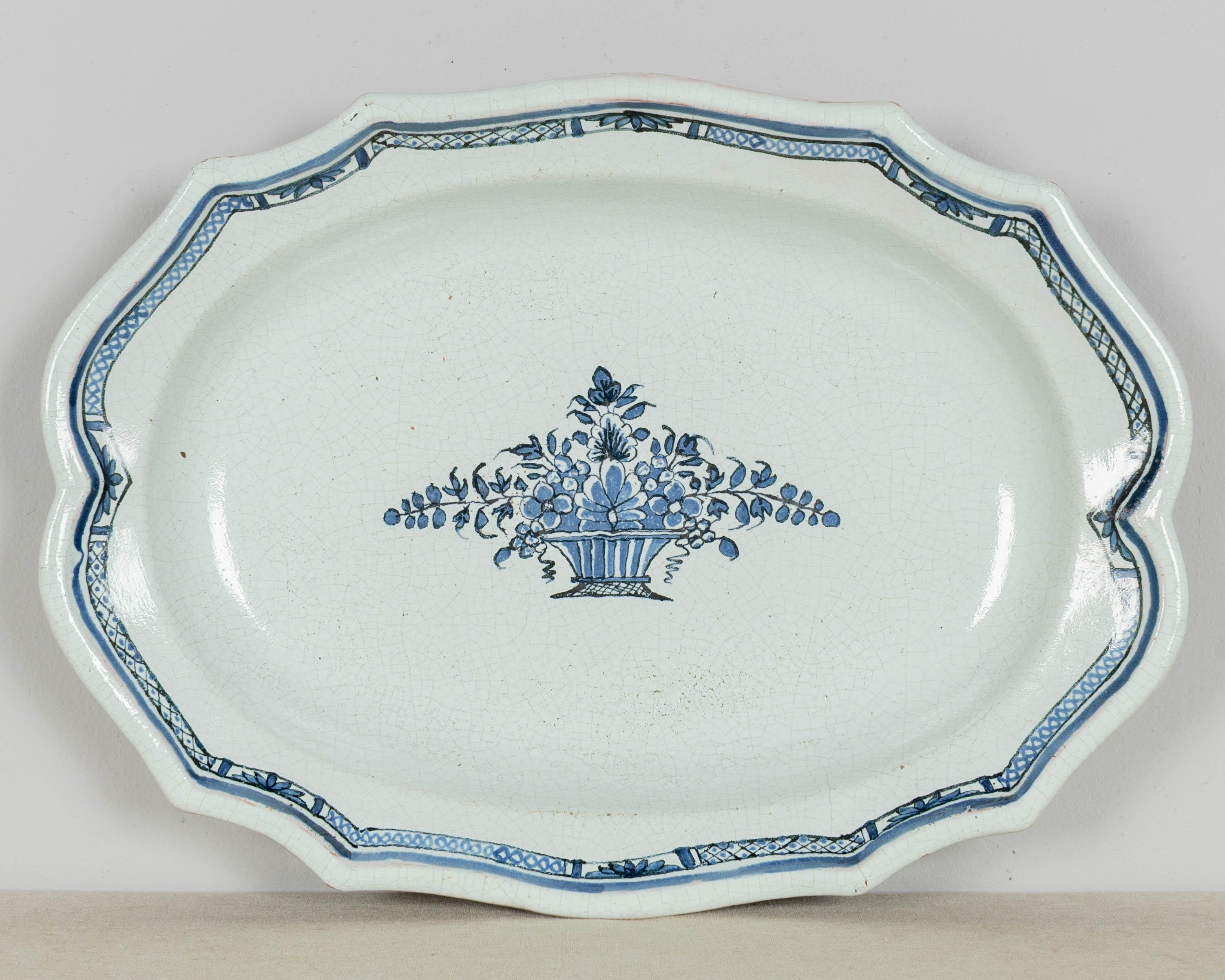 An 18th century French Rouen white glazed cul noir earthenware oval platter with scalloped edge, hand-painted with blue decorative banded border and a flower basket in the center. Robust heavy pottery with simple charming design and dark brown