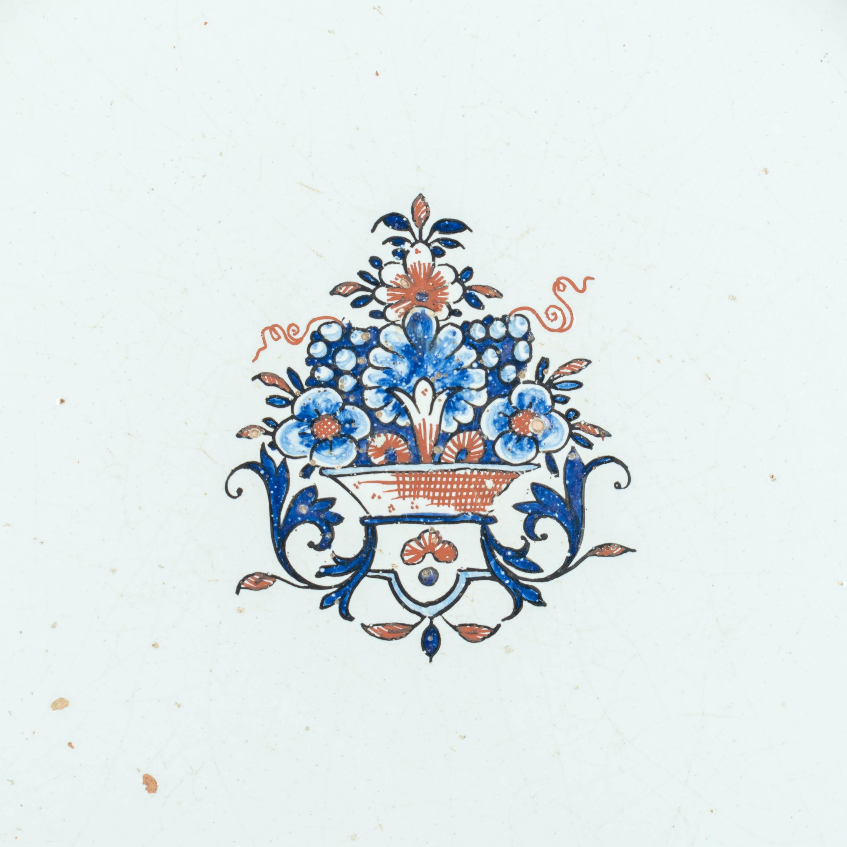 Ein großer weiß glasierter Steingutteller aus Rouen aus dem 18. Jahrhundert mit gebördeltem Rand, handbemalt mit blauen und roten Zierbändern und einem stilisierten Obstkorb in der Mitte. Robuste, schwere Töpferware mit einfachem, charmantem Design.
