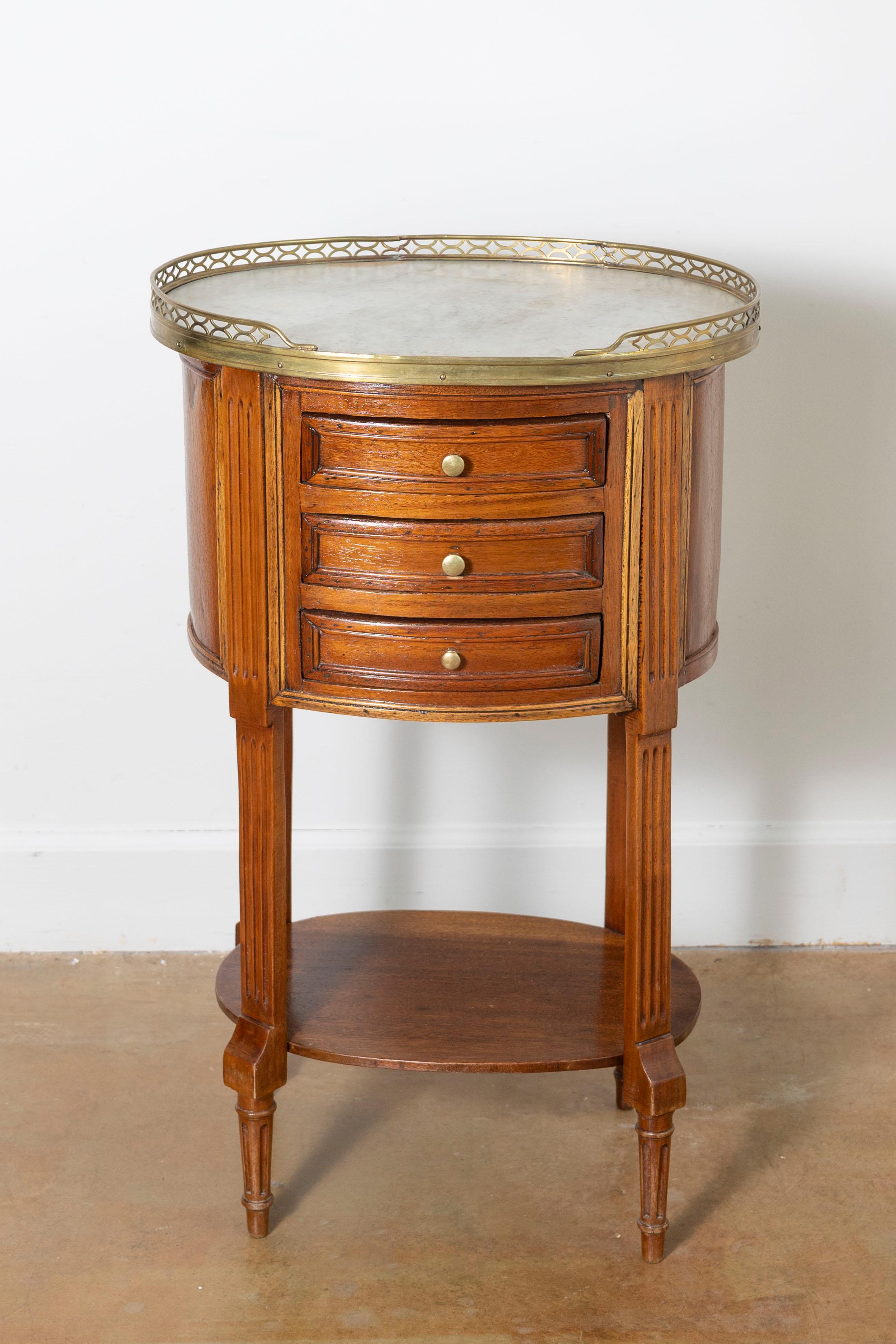 Cette table d'appoint française du XVIIIe siècle illustre l'élégance raffinée et le savoir-faire caractéristique du mobilier Louis XVI. Fabriquée en bois de noyer, la table présente un plateau arrondi avec une délicate galerie en laiton doré, ce qui