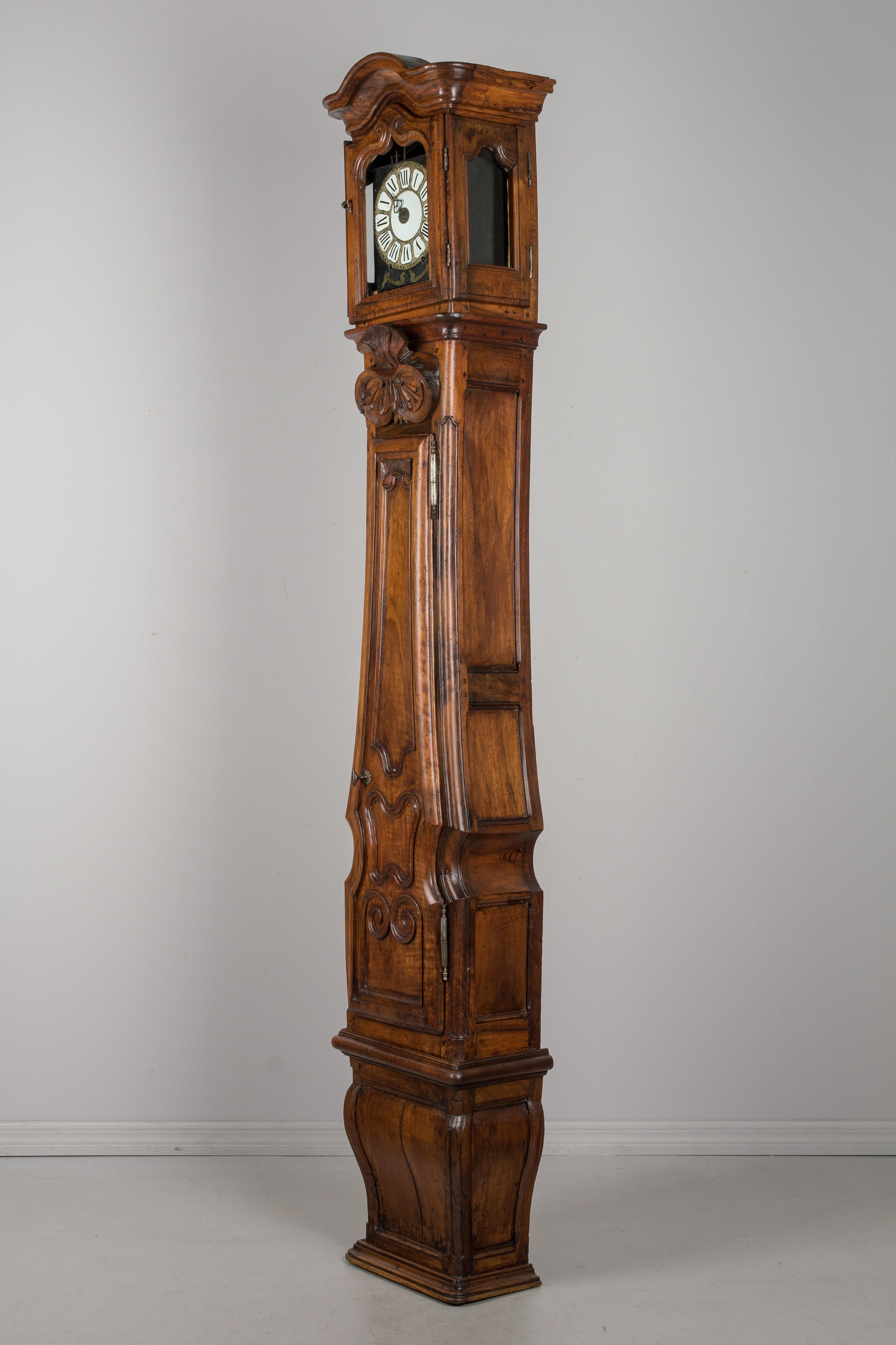 An exceptional 18th century French Horloge De Parquet, or tall case clock, from Lyon. Made of solid walnut and in three parts: a sturdy curved shaped base; the body with door panels carved into the wood; and top with original glass panes and chapeau