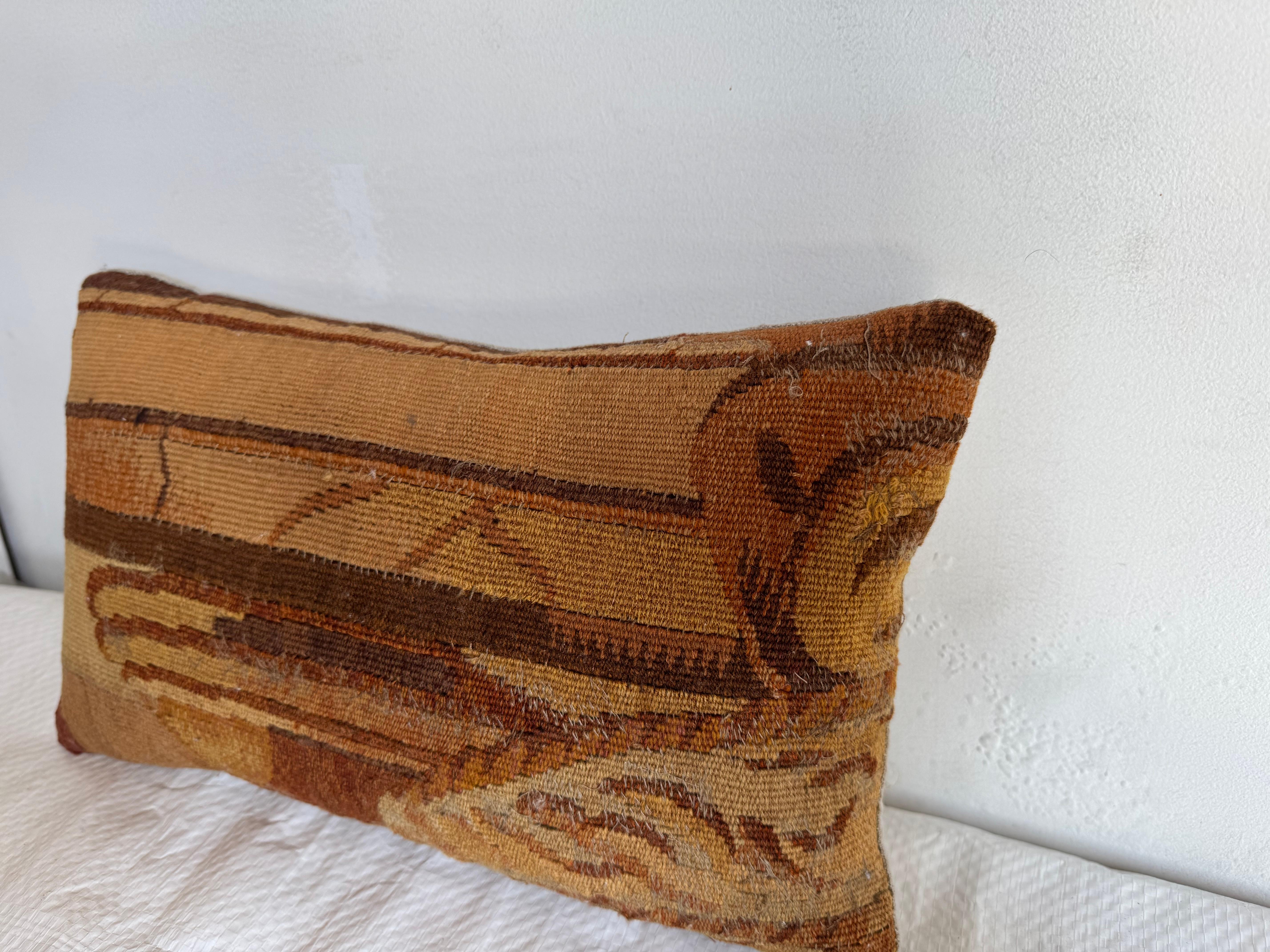Si tratta di un cuscino rettangolare in stile vintage realizzato con un antico tessuto da tappezzeria. Il cuscino presenta una tavolozza di colori terrosi con toni caldi di ruggine, ocra, marrone e marrone. Il disegno intrecciato comprende motivi