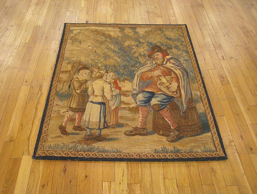 A framed French rustic tapestry from the 18th century, envisioning a pedant seated on a barrel, instructing a group children in music and the arts within a verdant setting. Enclosed by a narrow ribbon-twist border. Wool with silk inlay. Measures: