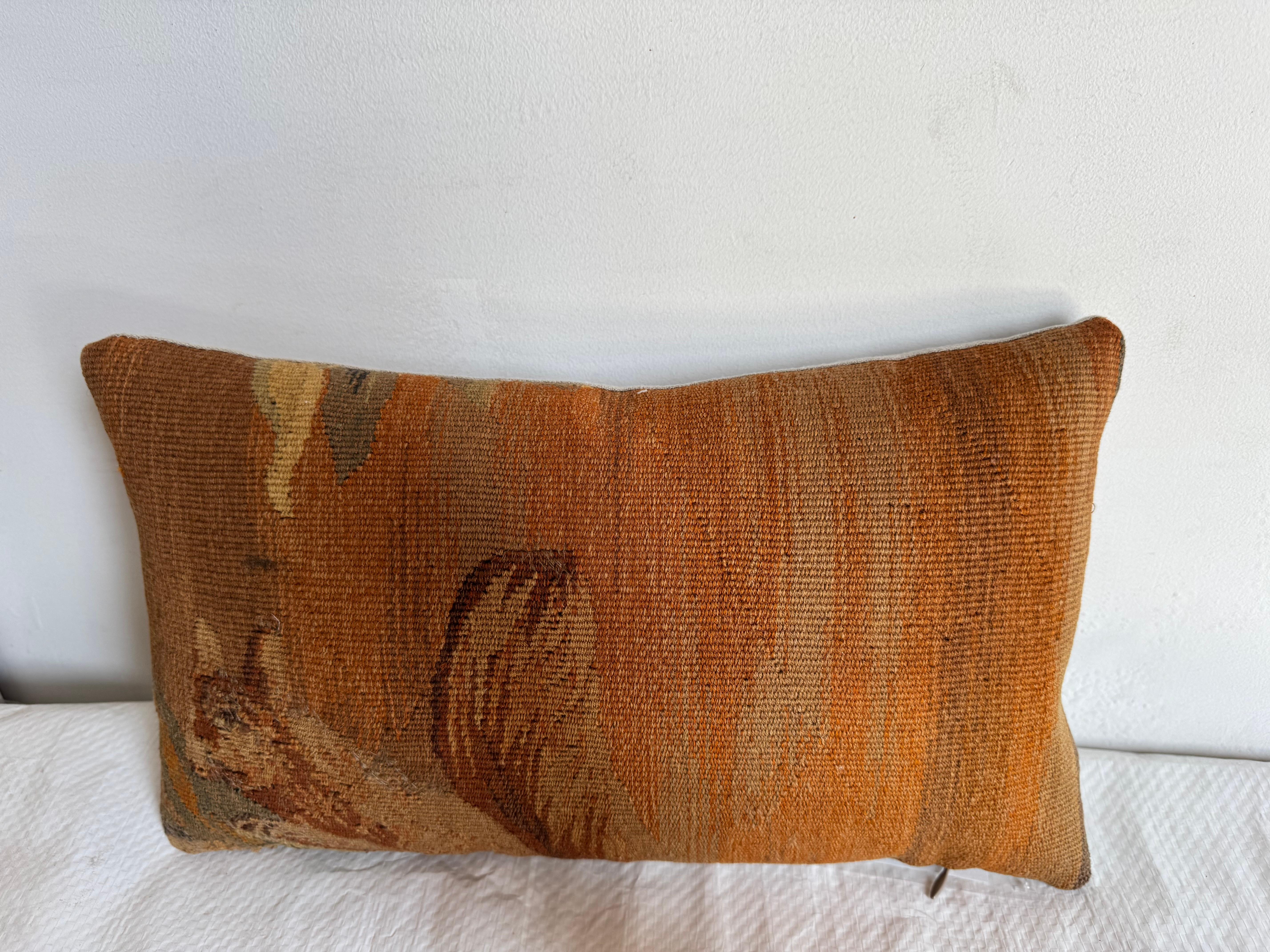 Questo cuscino è un arazzo vintage in stile Aubusson con un'eleganza sottile e terrena. Il cuscino è caratterizzato da una tenue tavolozza di arancione bruciato, terra di Siena, ocra, marrone tenue e salvia, che forma una scena pastorale leggermente