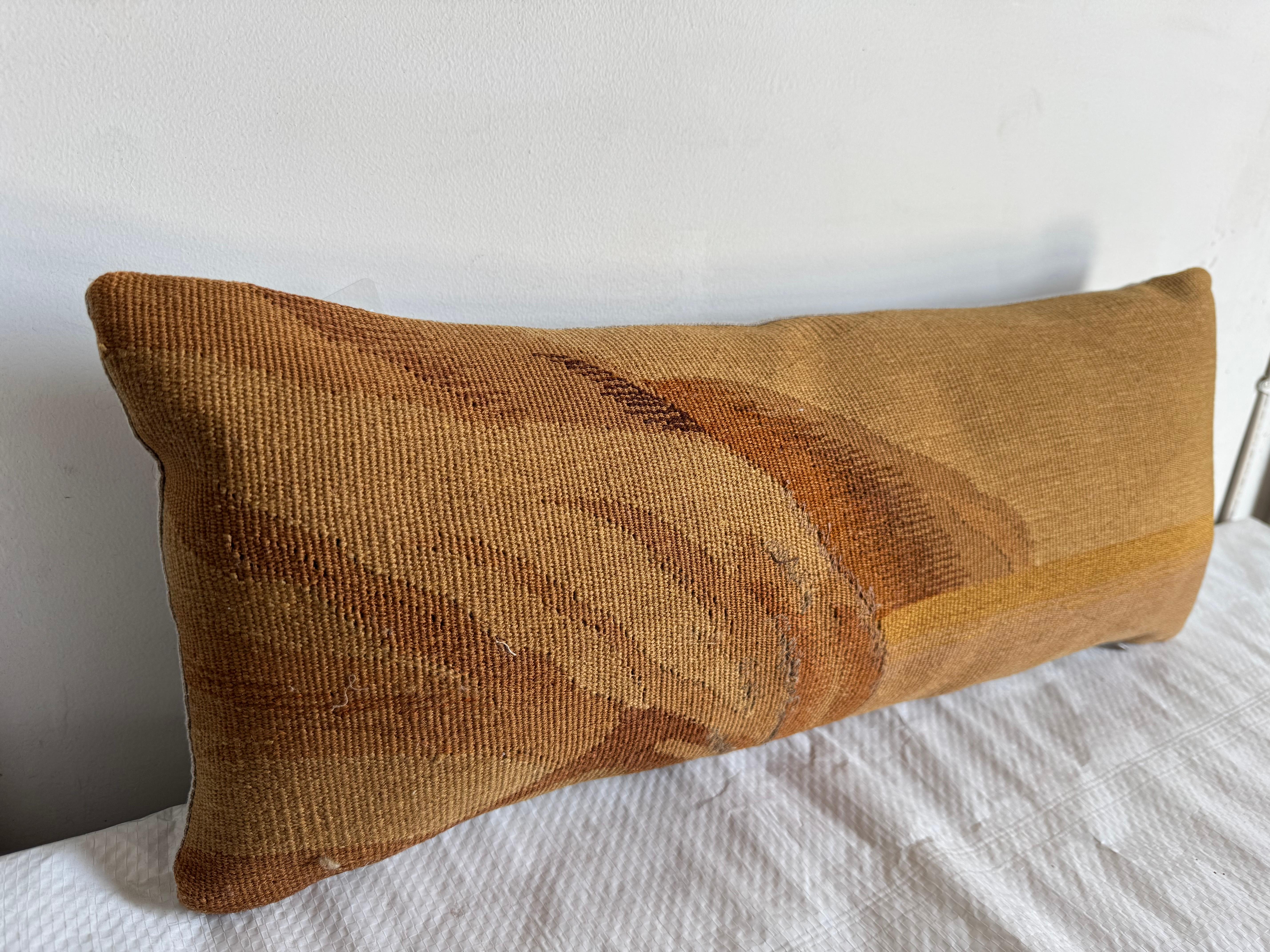 Un refinado cojín de tapiz francés de Aubusson del siglo XVIII, que muestra un raro motivo abstracto en tonos cálidos y terrosos. Tejido a mano en lana y revestido con un tejido neutro, este cojín lumbar alargado incorpora una suave inserción de