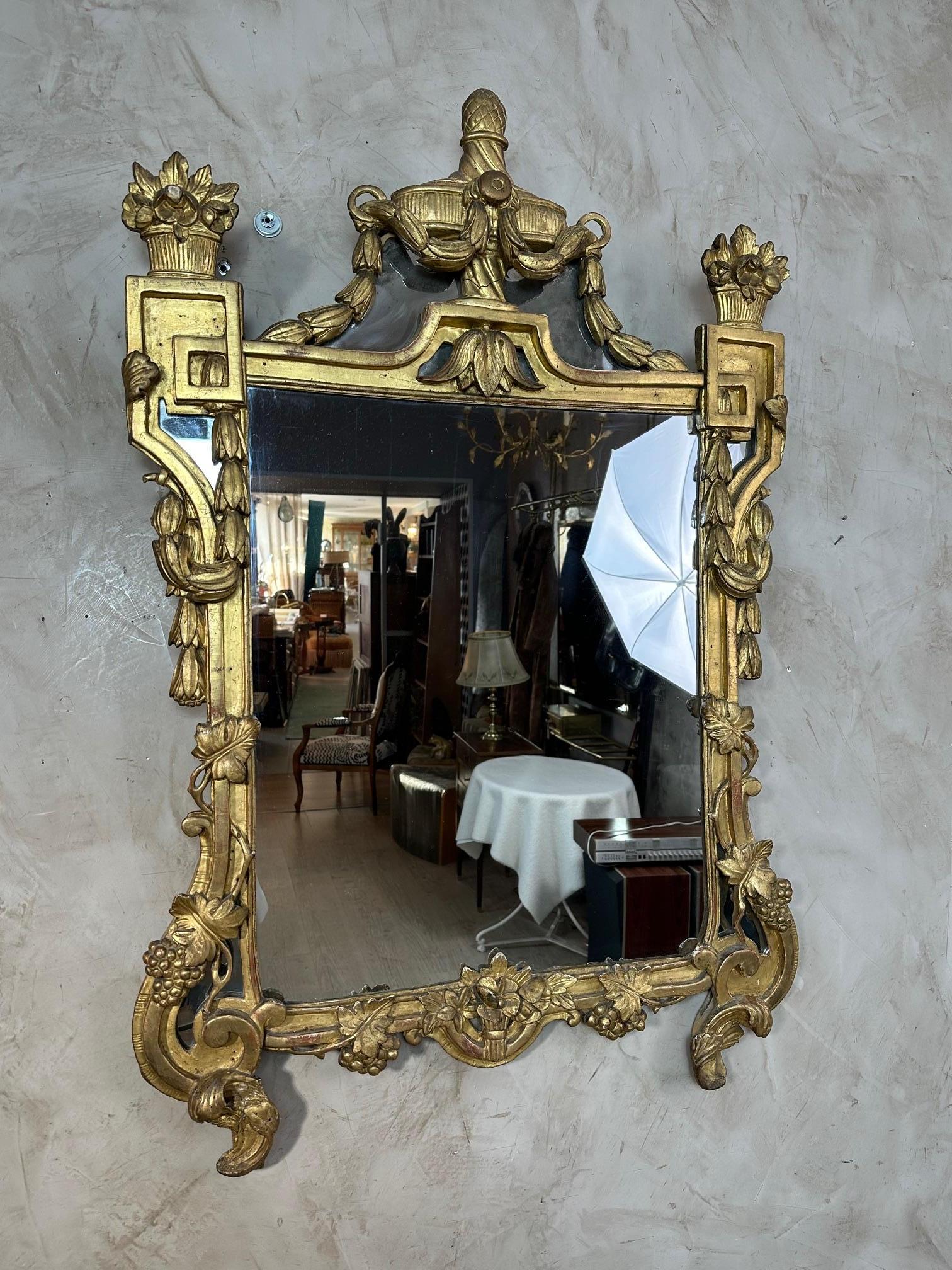 Magnifique miroir en bois doré datant du XVIIIe siècle, caractéristique de la période de transition Louis XV-Louis XVI.
Son décor finement sculpté combine avec élégance des volutes rococo adoucies, des guirlandes feuillues, des rubans et des motifs