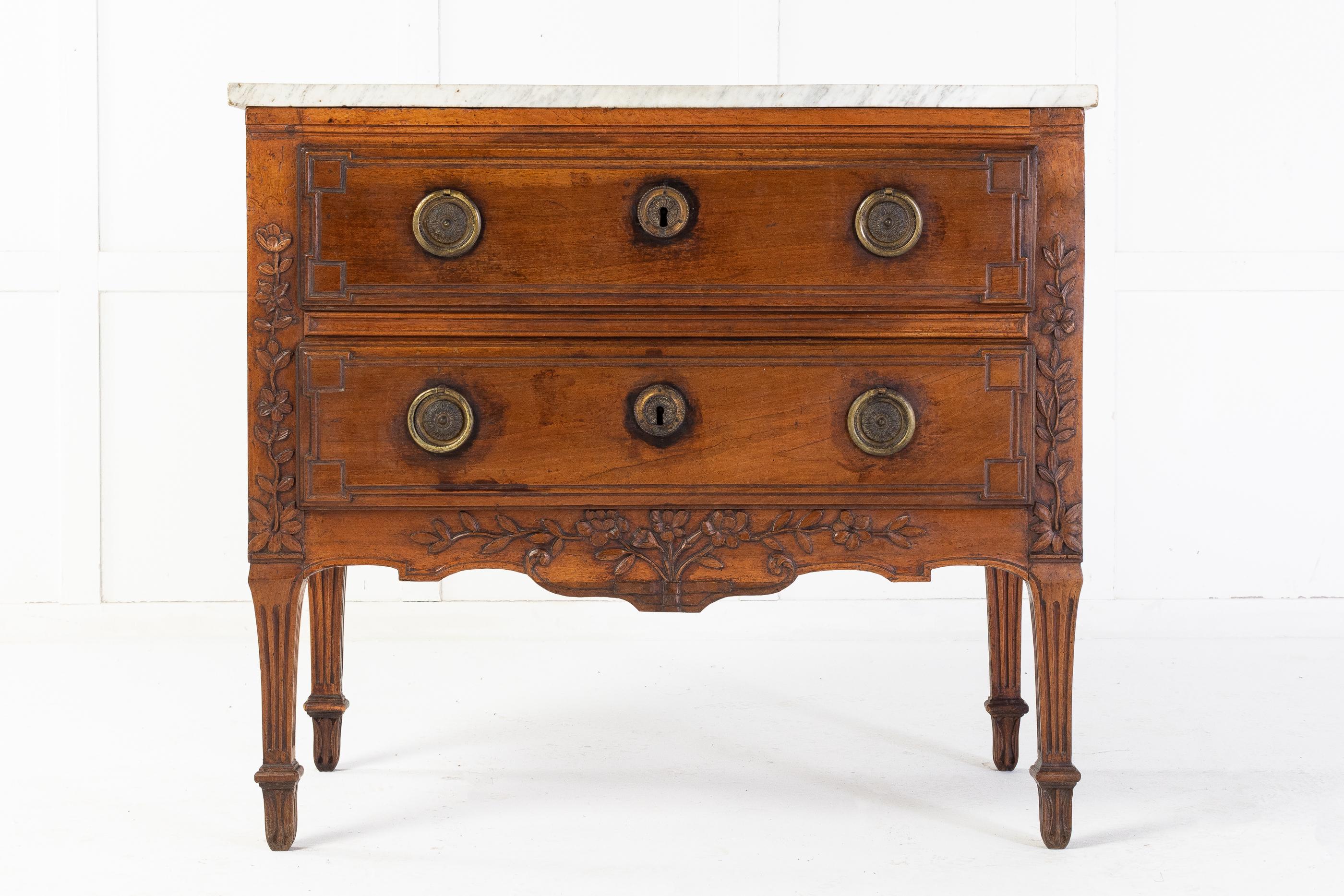 18th century French, walnut two drawer commode of nice proportions with a white marble top. The two moulded drawers are flanked by carvings of a floral design, above a carved shaped apron with similar floral design. Standing on shaped and fluted