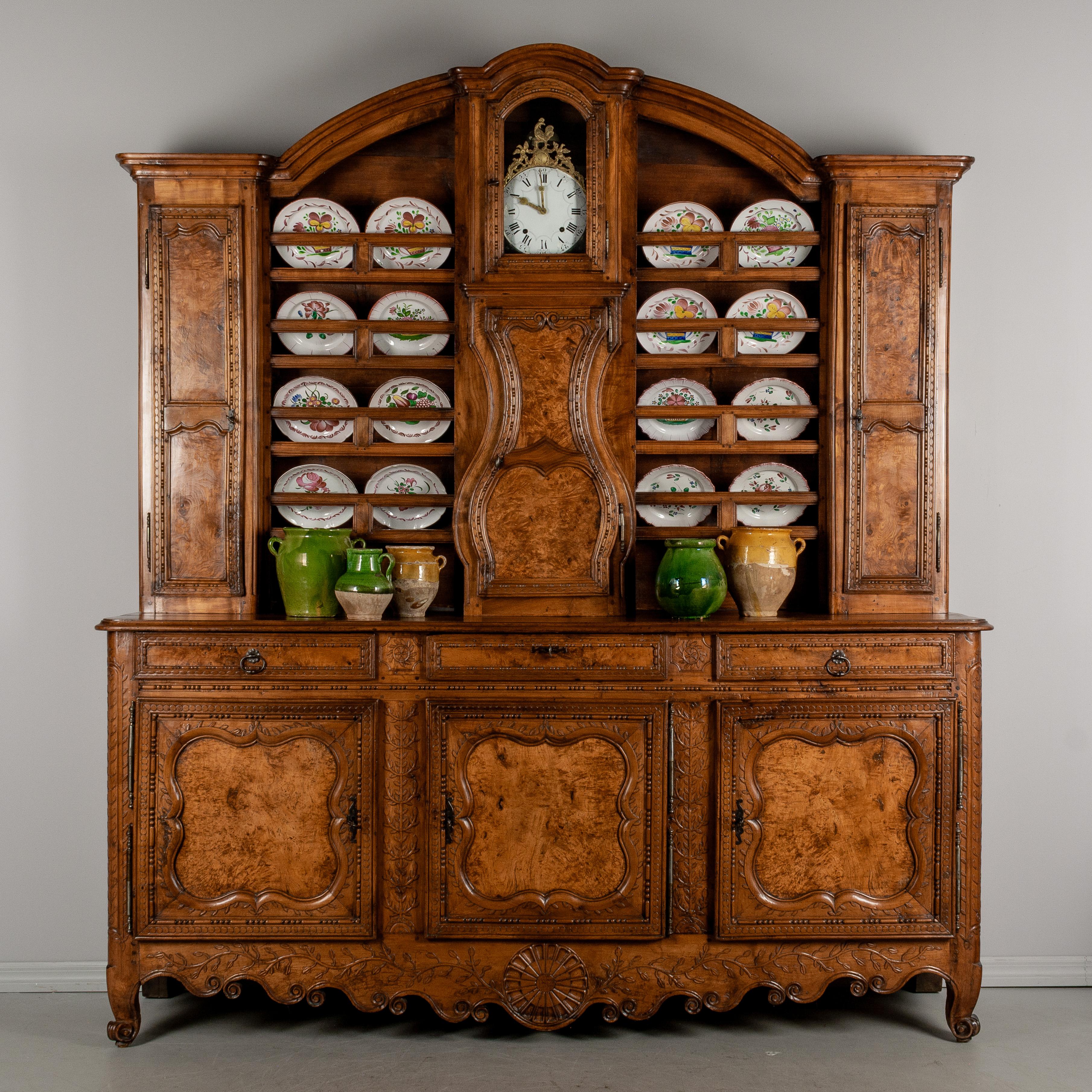 An 18th century Country French vaisselier from Burgundy comprised of a large buffet and a china hutch with clock. Made of solid cherry and walnut and highly decorated with hand-carved vines framing beautifully patterned burl of elm wood panels.