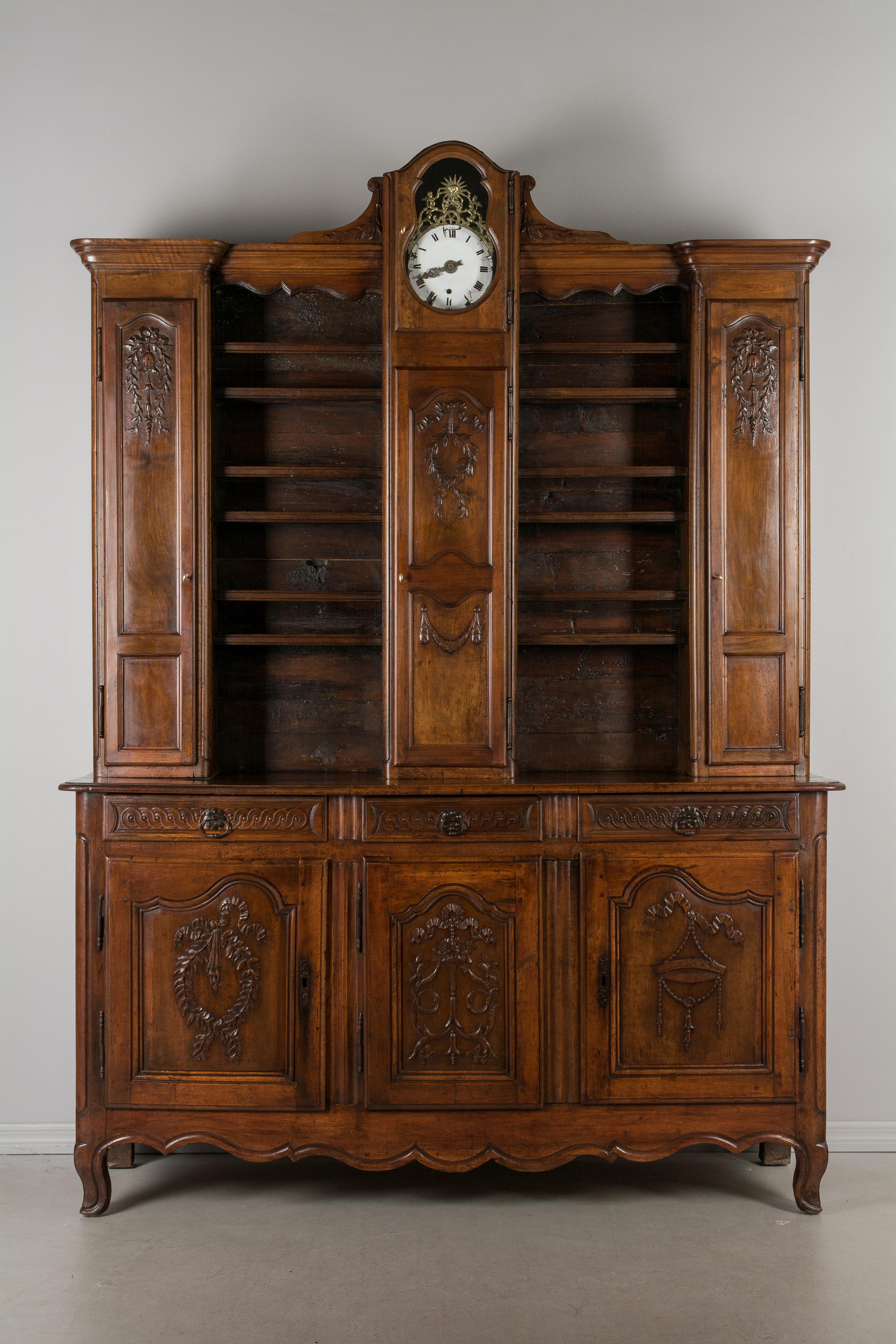 A late 18th century country French buffet vaisselier from Burgundy made of solid walnut beautiful hand carved decoration of flowers, ribbons and wreaths. The hutch has the original clock with enamel face and cast brass surround and is in working