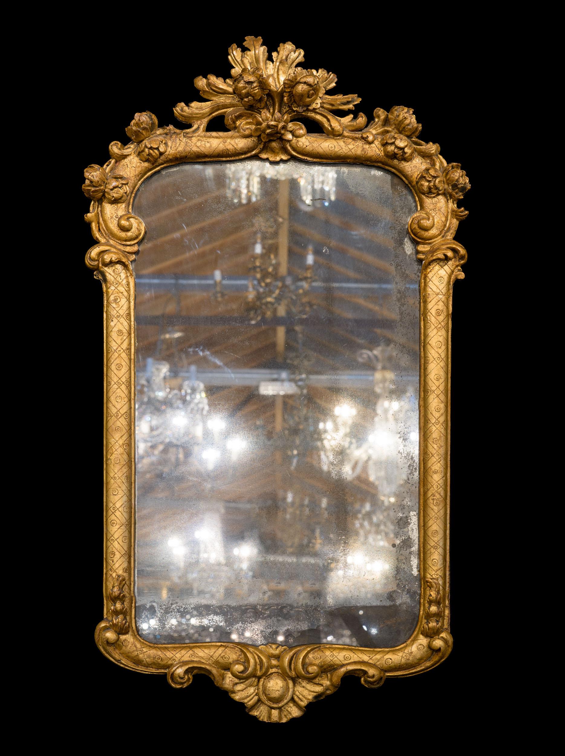 A charming eighteenth century wall mirror with an ogee shaped giltwood frame, surmounted by a foliate and floral crest comprising oak leaves and roses. These trail over the scrolled shoulders, the rest of the frame decorated with cross hatching.