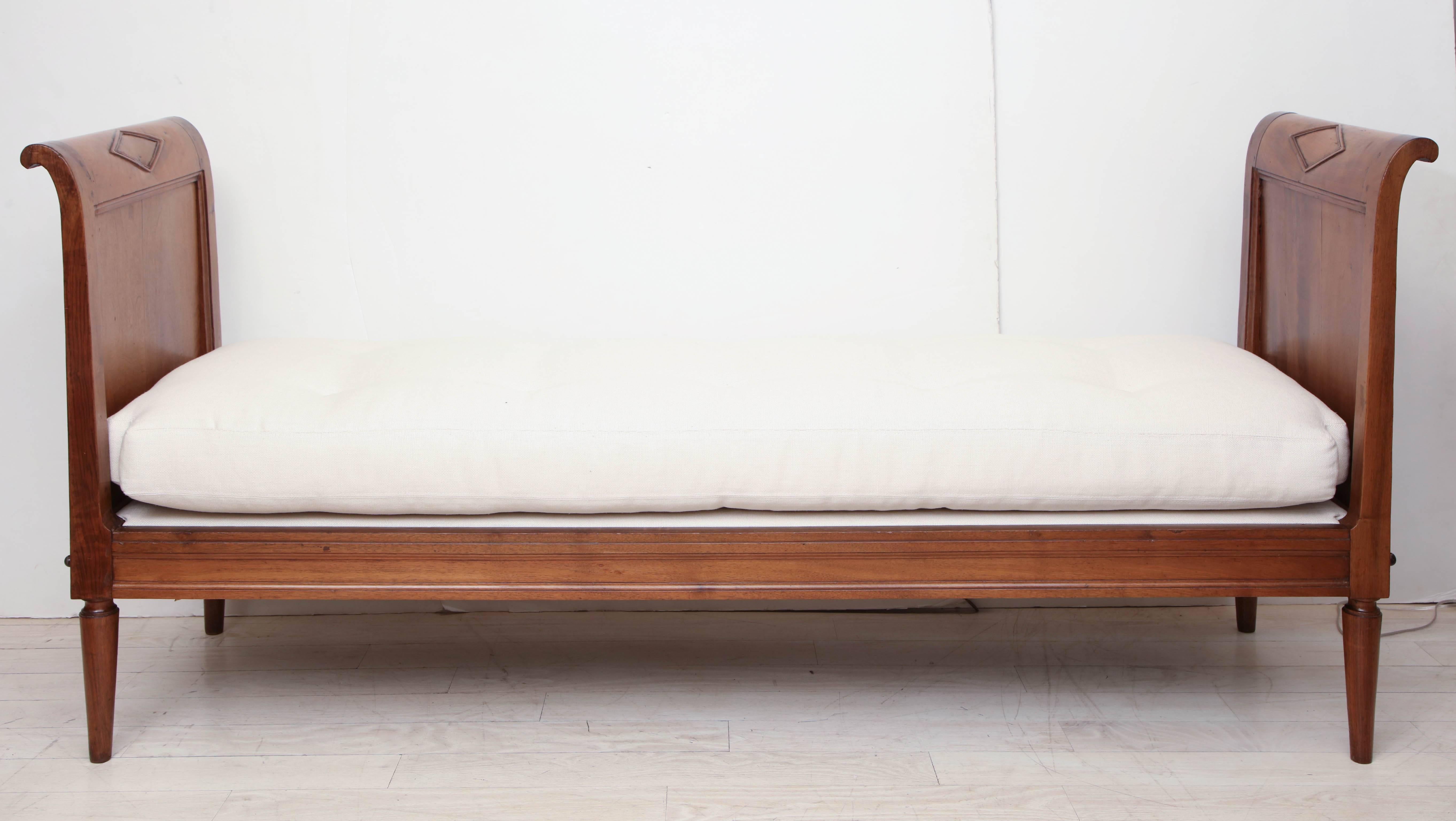 An 18th century walnut daybed with curved, paneled sides and carved detail. Newly upholstered in tufted Belgian linen.