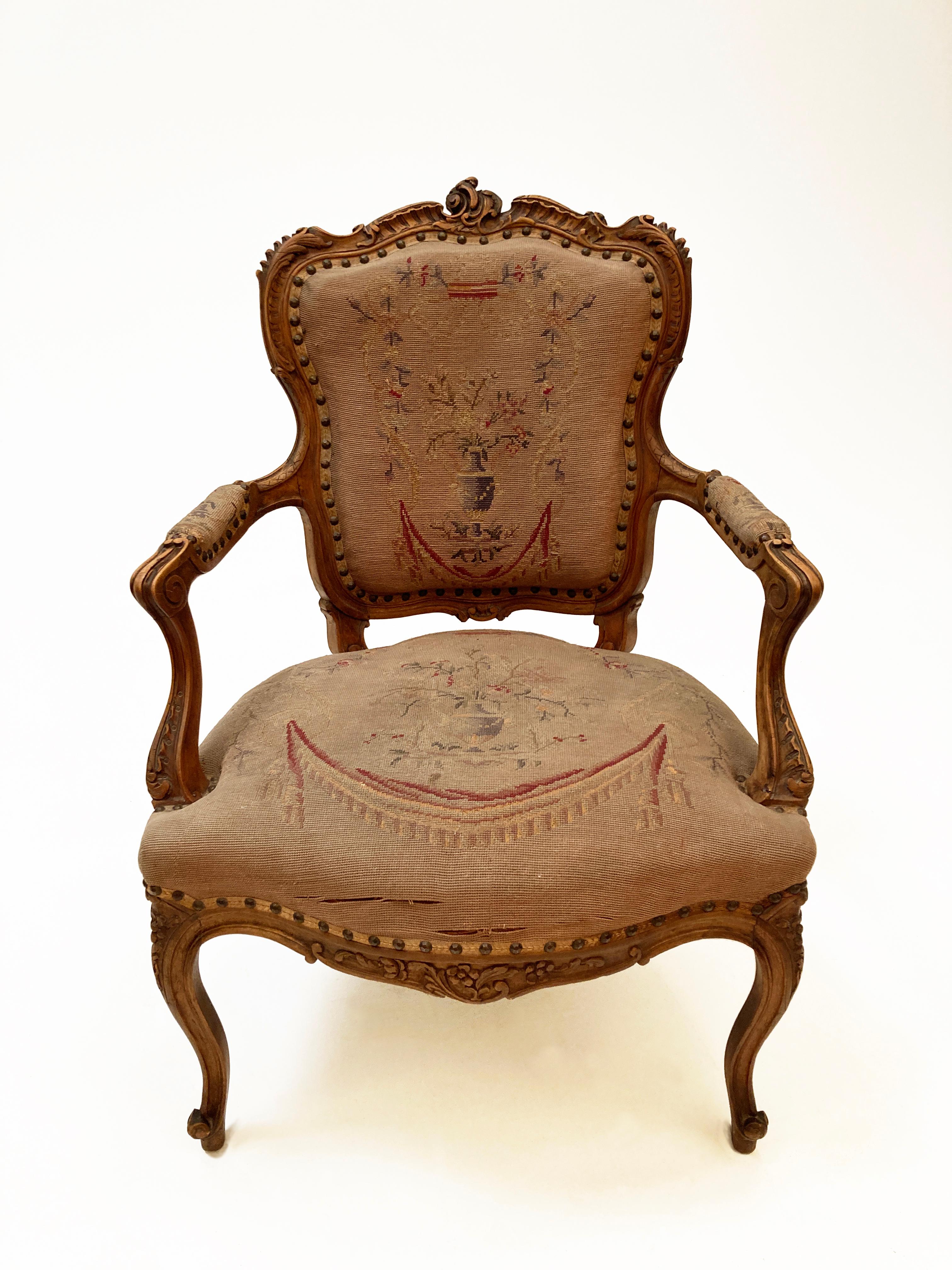This mid 18th century French Louis XV walnut fauteuil with seemingly gloriously original upholstery portrays an exquisite petit-point that shows beautiful aging and a few minor areas that are reparable. The chair frame encompassing the padded back,