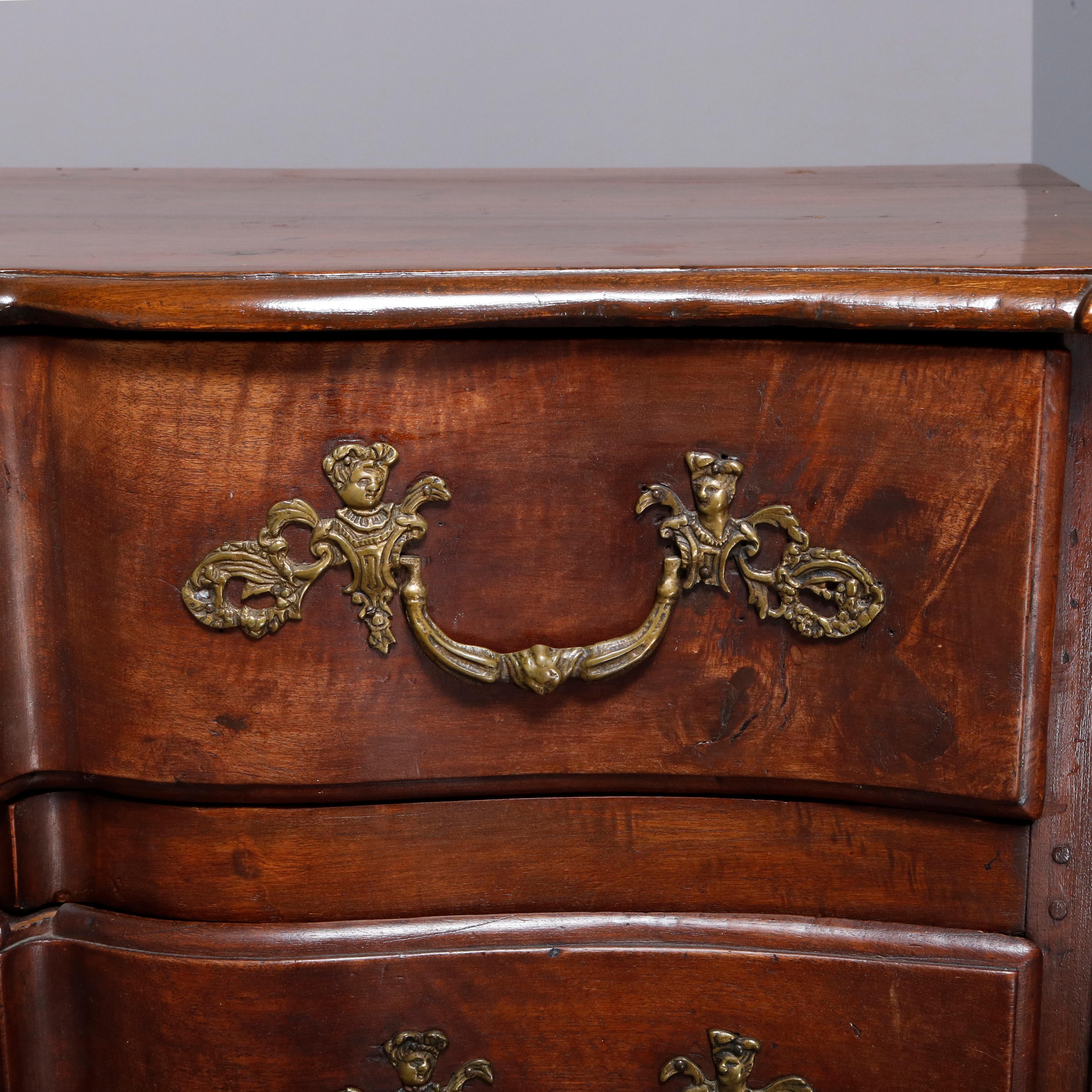 An 18th century antique French commode offers walnut pegged and paneled construction with shaped top surmounting serpentine case having three long drawers each with figural cherub cast bronze hardware, 19th century. 

***DELIVERY NOTICE – Due to