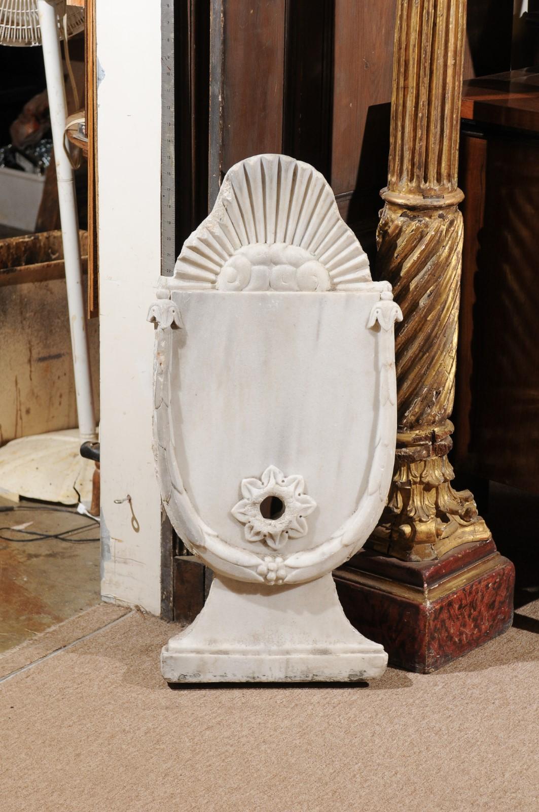 A beautifully carved white Carrara marble wall fountain head from 18th Century France with a fluted top, rounded body, with carved leaf border detail, circular spout and splayed base.