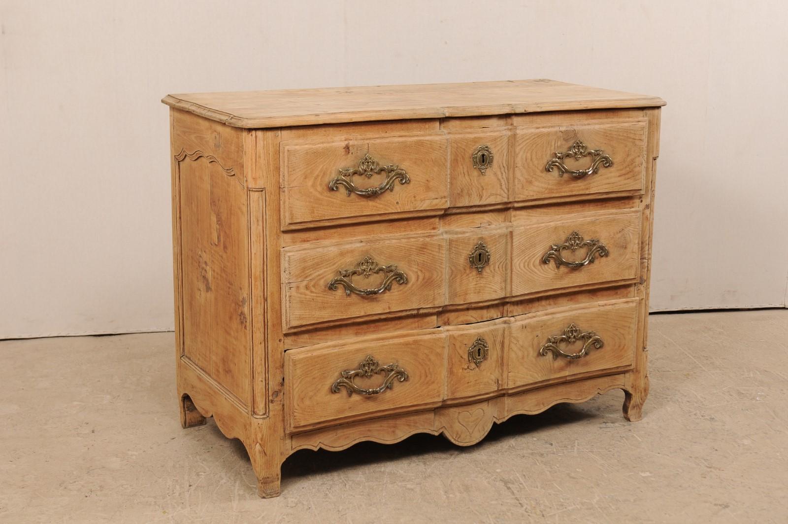 An 18th century French chest of three drawers. This antique commode from France features a delicate oxbow-front, carved and rounded front posts, decoratively carved single recessed panel sides, and a scalloped skirt at three sides with heart-shaped