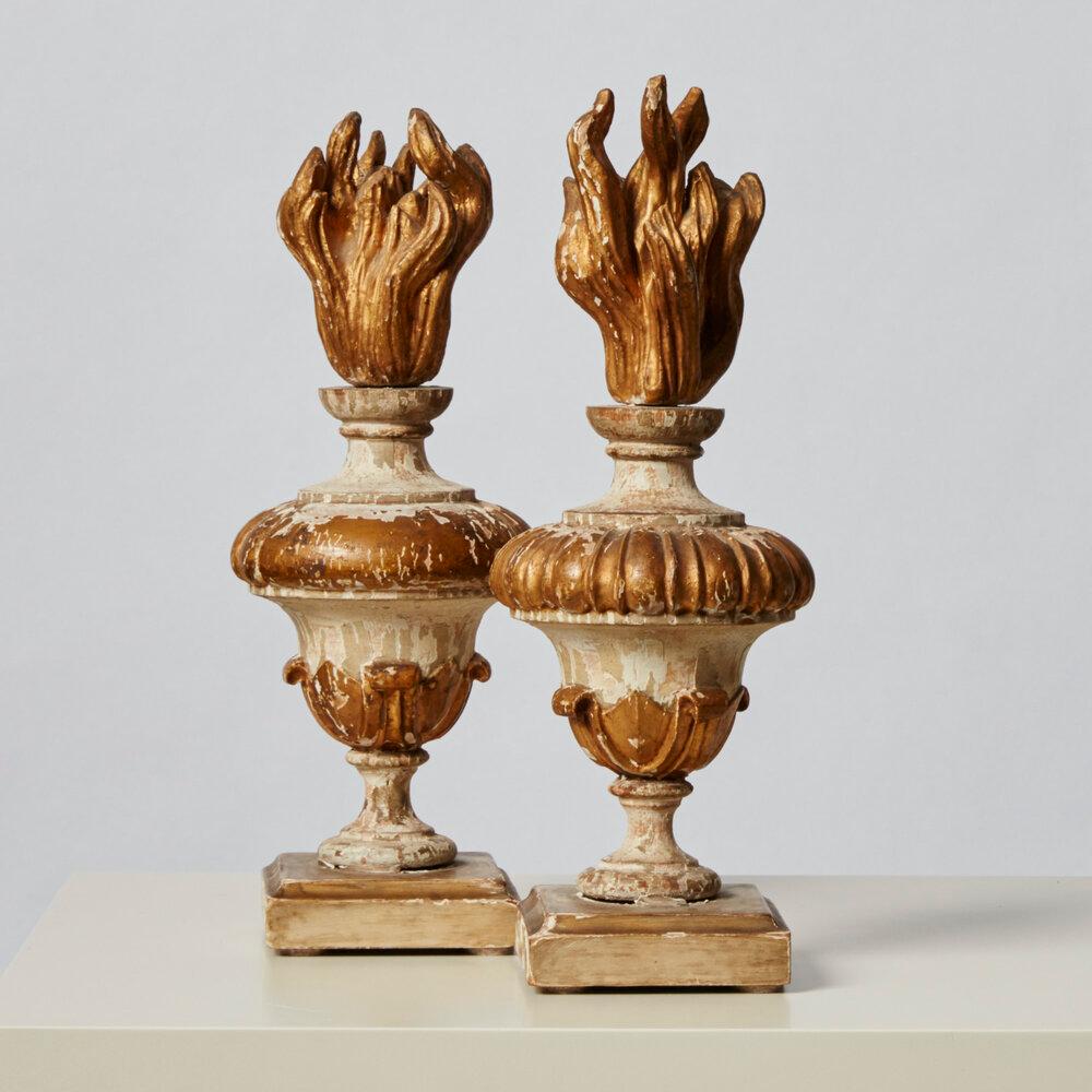 Pair of gorgeous decorative urns topped with flame-shaped finials. Hand painted, gilt gesso and hand carved wood detailing. They feature a carved vase with a gadroon detail and a flame finial typical of 