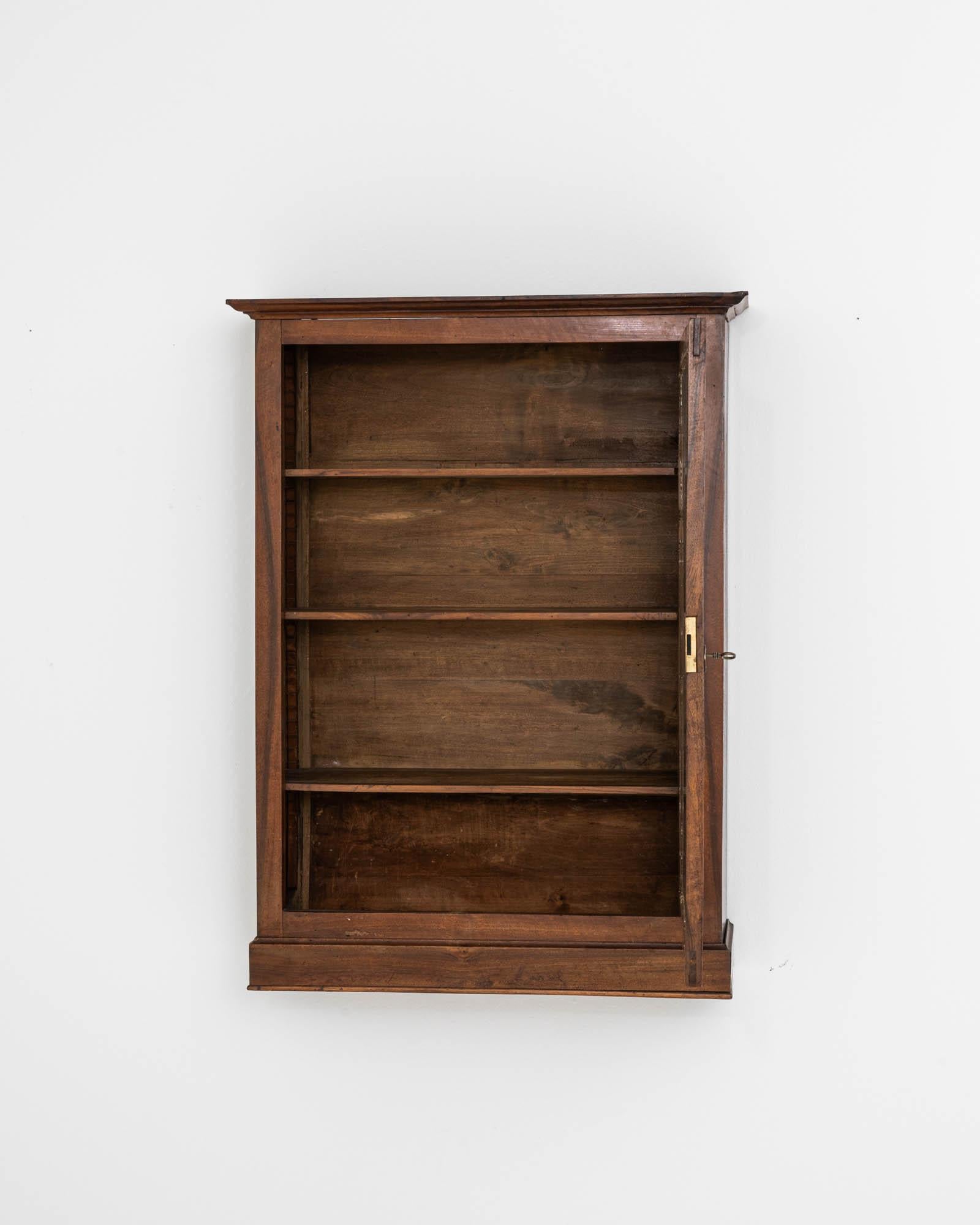 This 18th Century French Wooden Wall Vitrine is a rare gem, steeped in history and crafted with the utmost care. Its aged wood frame boasts a deep, lustrous patina that only centuries can bestow, and the delicate glass front elegantly displays your