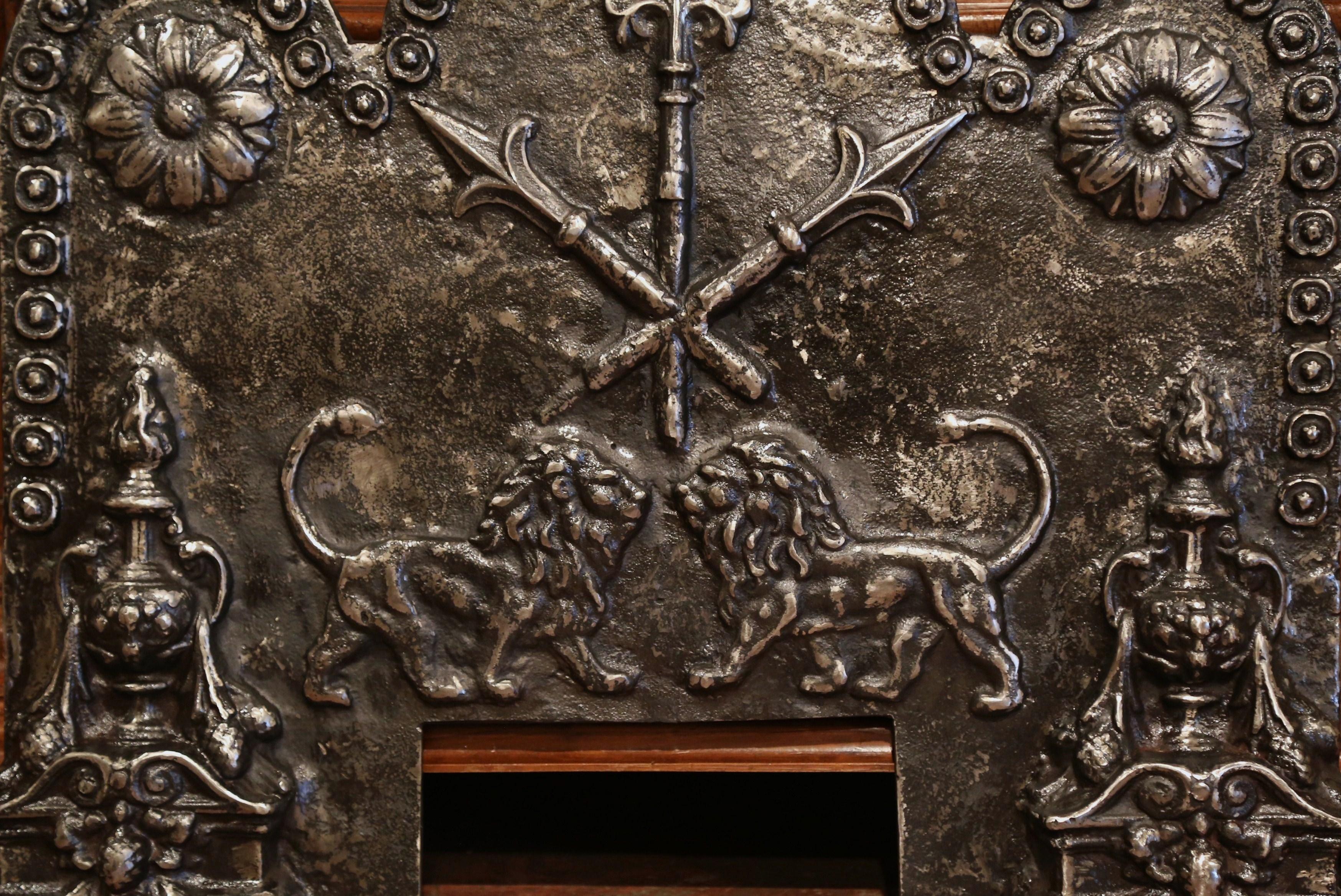 This large antique iron fire back was crafted in France, circa 1780. The heavy plaque features three elegant arches with round medallions in each corner, the fire back is decorated with a pair of roaring lions facing each other with crossed spears,