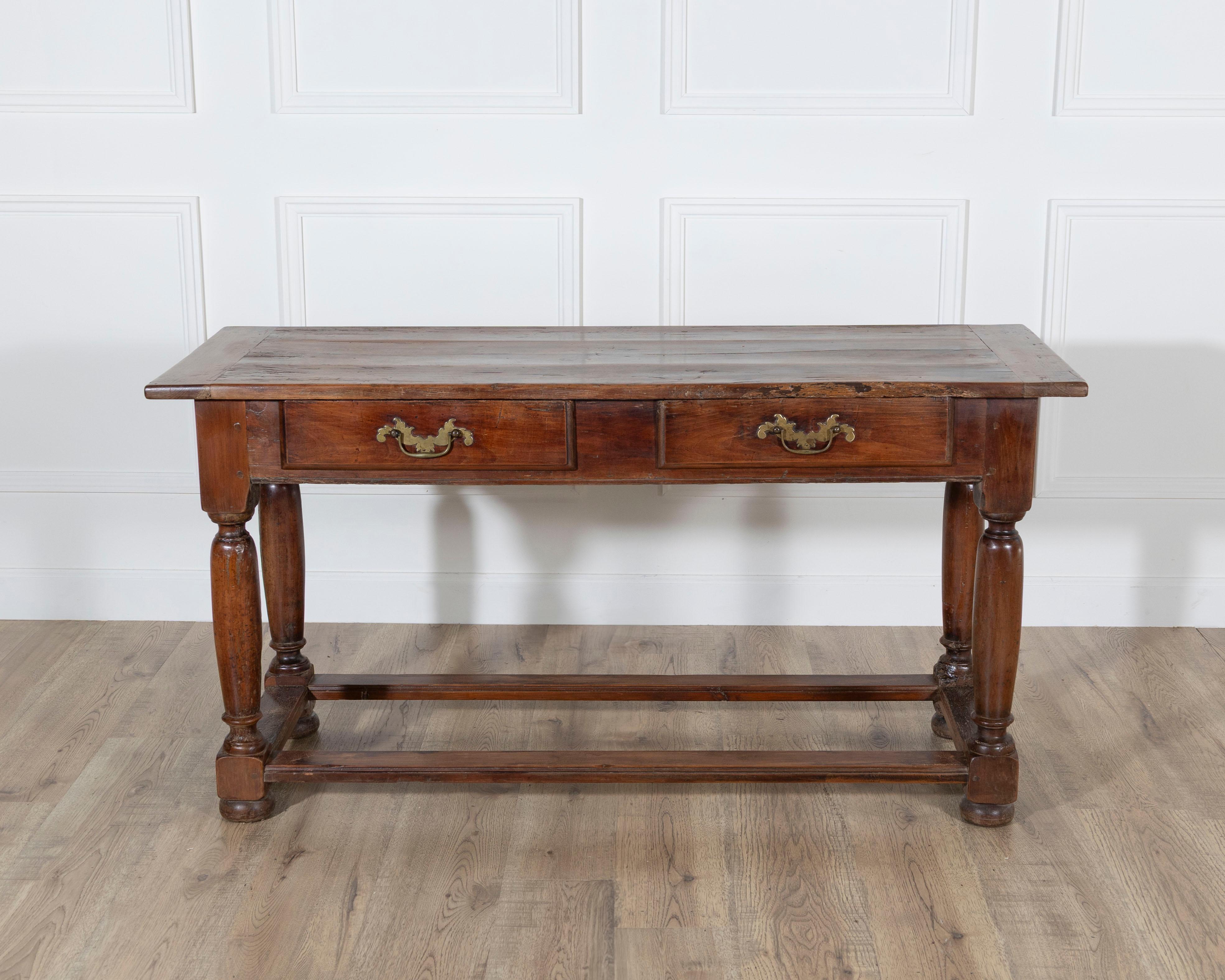 Una refinada consola del siglo XVIII realizada en madera maciza de frutal bellamente envejecida, que muestra los tonos cálidos y la profundidad natural característicos de la época. La encimera rectangular descansa sobre dos espaciosos cajones, cada