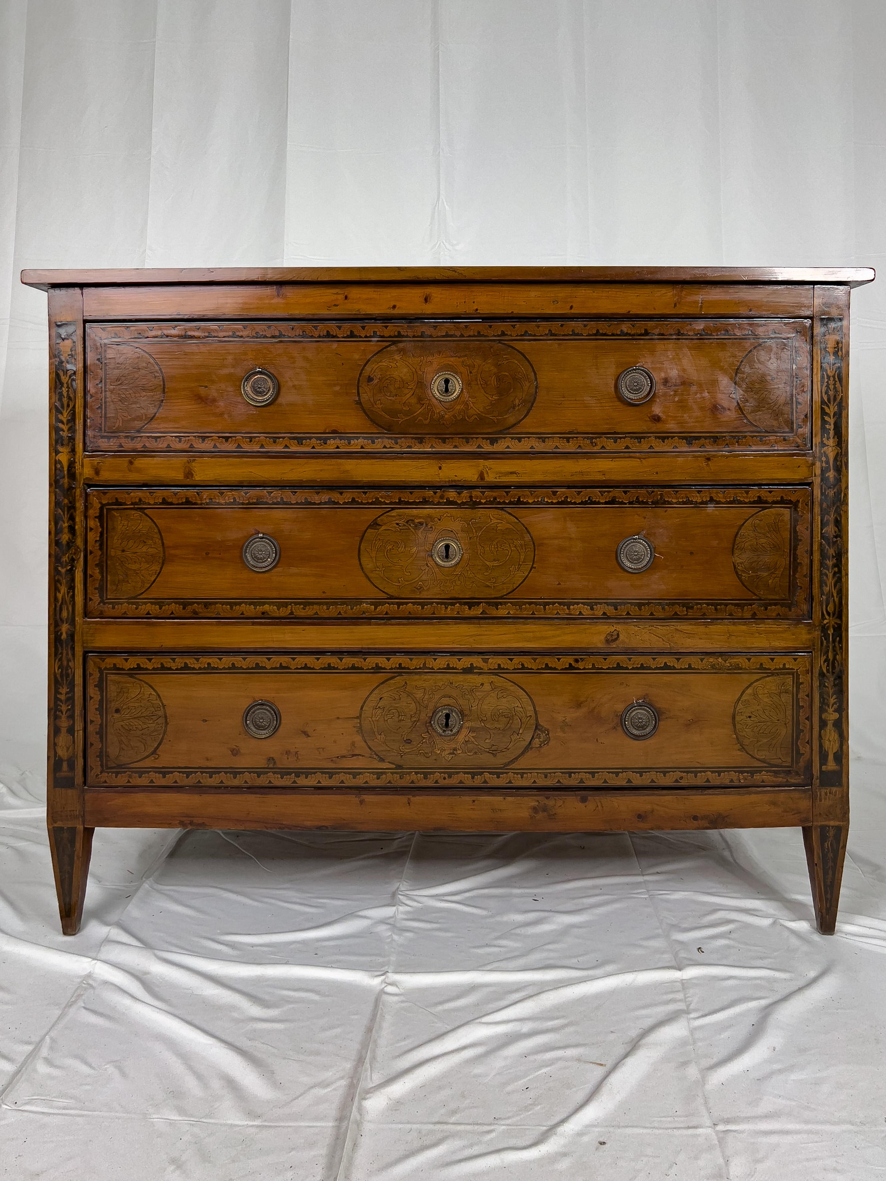 18th century 3 drawer fruitwood Italian commode with walnut inlay on the top, front, legs and sides of the piece. The inlay depicts urns in the medallions and foliate designs in the corners. Every surface of the commode has a rich patina. This piece