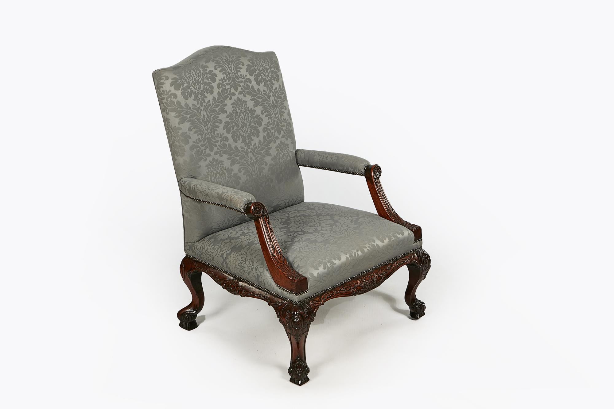 18th century Gainsborough armchair in the manner of Chippendale with ribbon carved apron supported by cabriole leg adorned with C-scroll motif terminating on scroll foot with acanthus leaf carving.