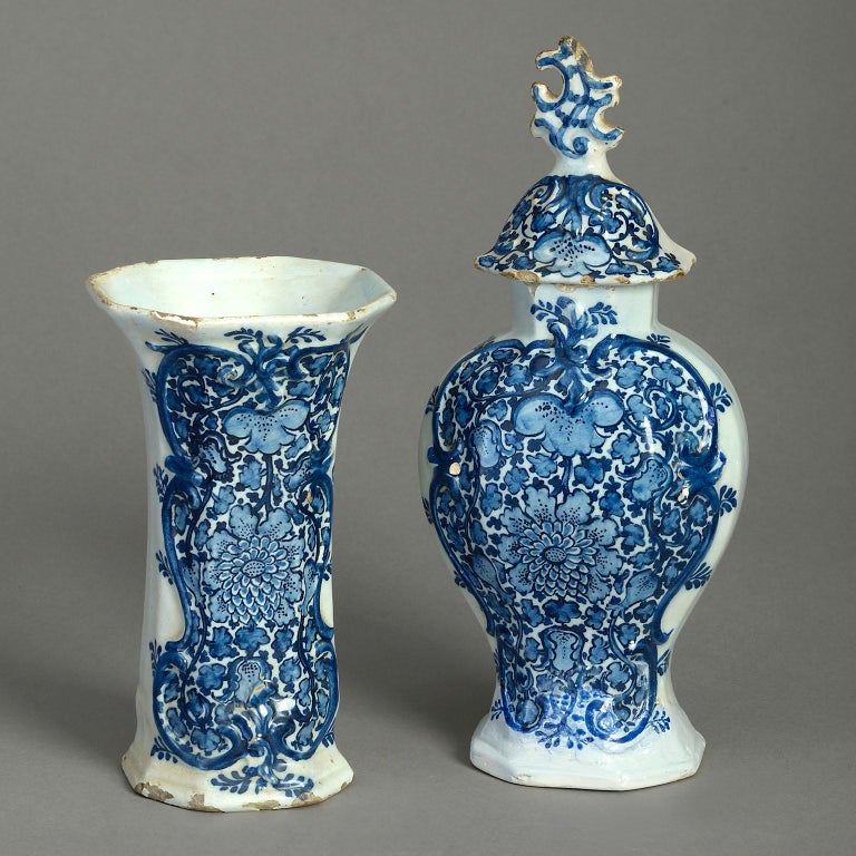 A late 18th century garniture of five blue and white glazed Delft pottery vases, the lids with scrolling finials, the bodies of baluster and trumpet form, decorated with intricate floral and foliate work within C-scrolls. With maker’s marks to the