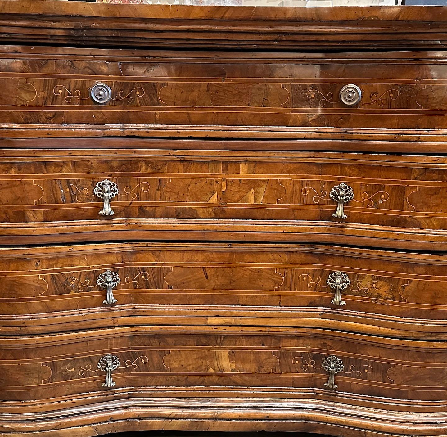 Unusual, hand carved, veneered, inlaid and ebonized, four drawer, serpentine front commode with clipped corners bolstered by turned pilasters capped with Corinthian capitals. The whole in Burl veneer with foliate style, pear wood inlay. Original,