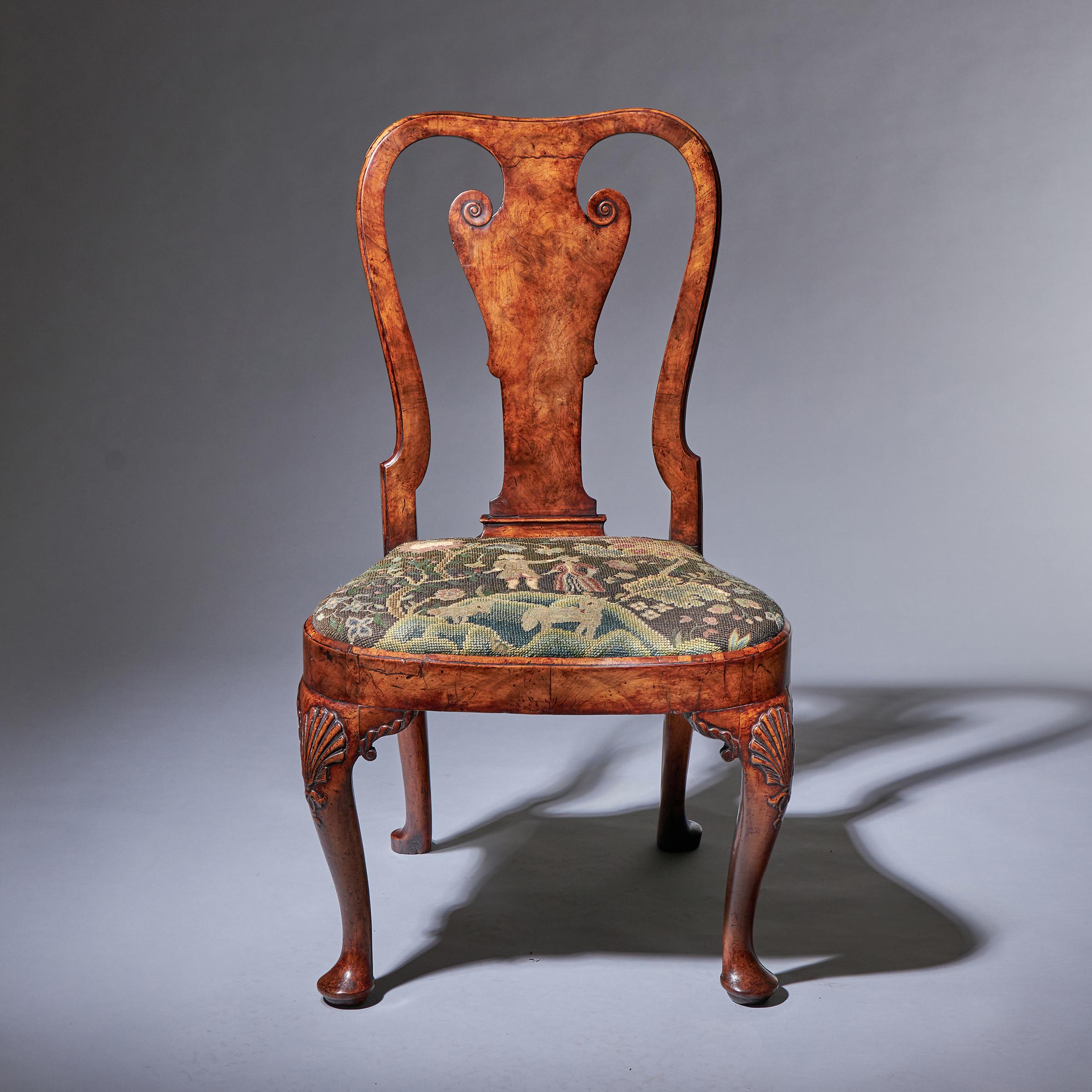A superb early 18th-century George I carved walnut chair, circa 1720. England 

The figured walnut volute carved violin splat terminates to a fixed moulded shoe and is most elegantly flanked by cascading s-scroll styles. The bell-shaped seat is