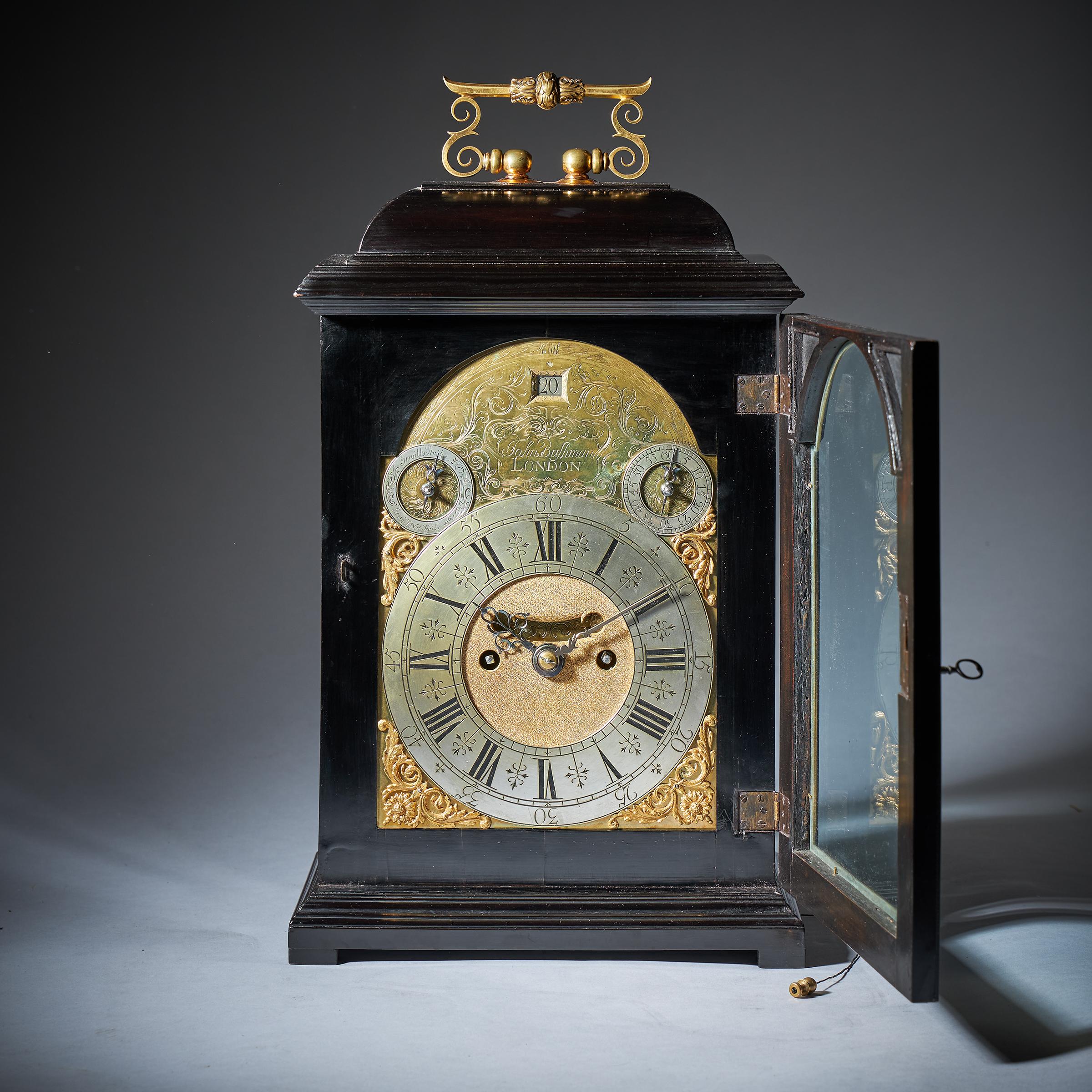 This great early arched spring clock has a 7-inch dial with unusual flower and scroll spandrels, matted centre with mock pendulum aperture. The upper corners have two subsidiary dials for strike/silent and regulation. The foliate engraved arch with