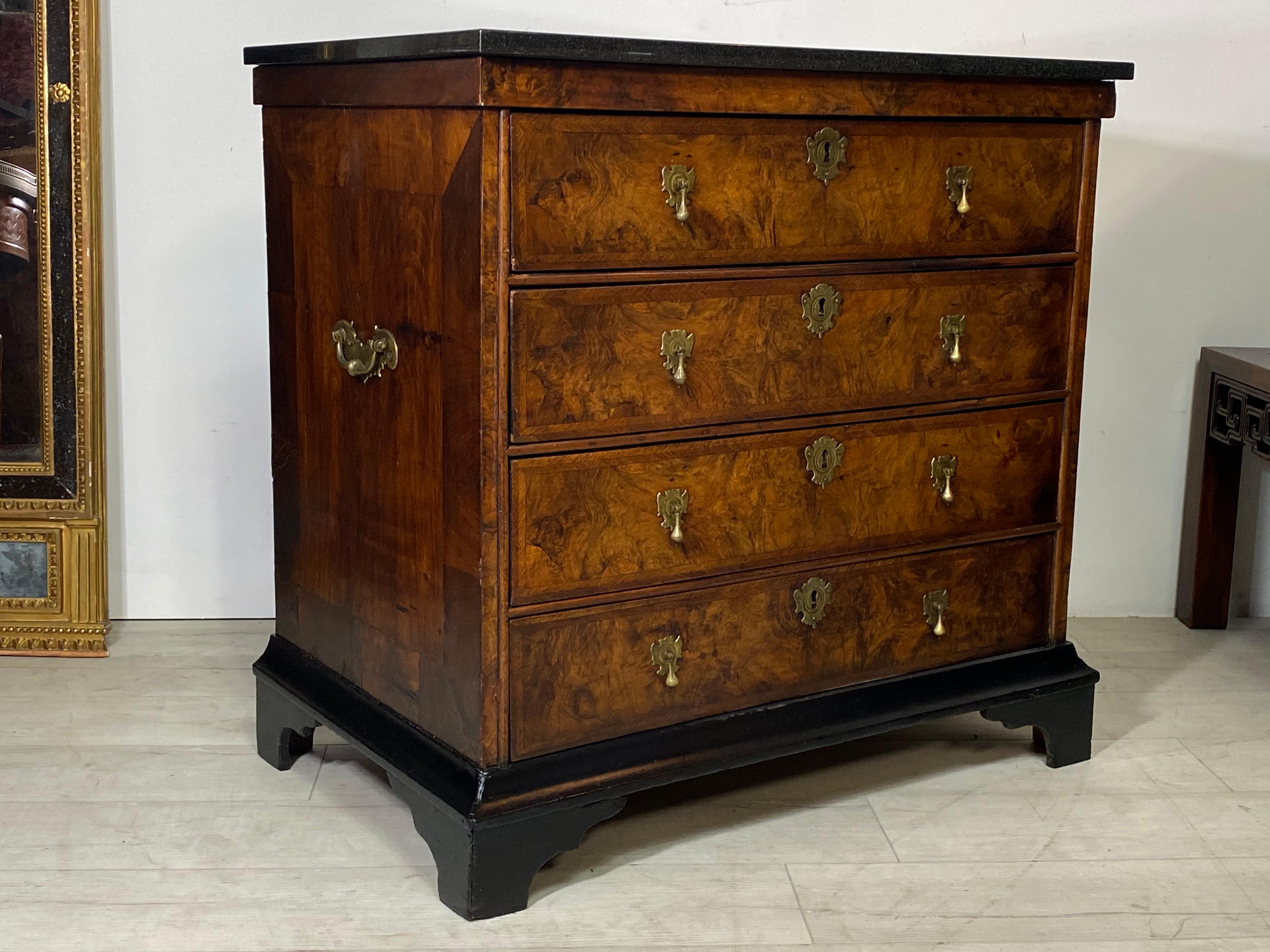 18th century George I English walnut veneered chest of drawers with original brass pulls and brass bale handles on the sides on a repainted black bracket base. New black granite top (was likely marble, originally).