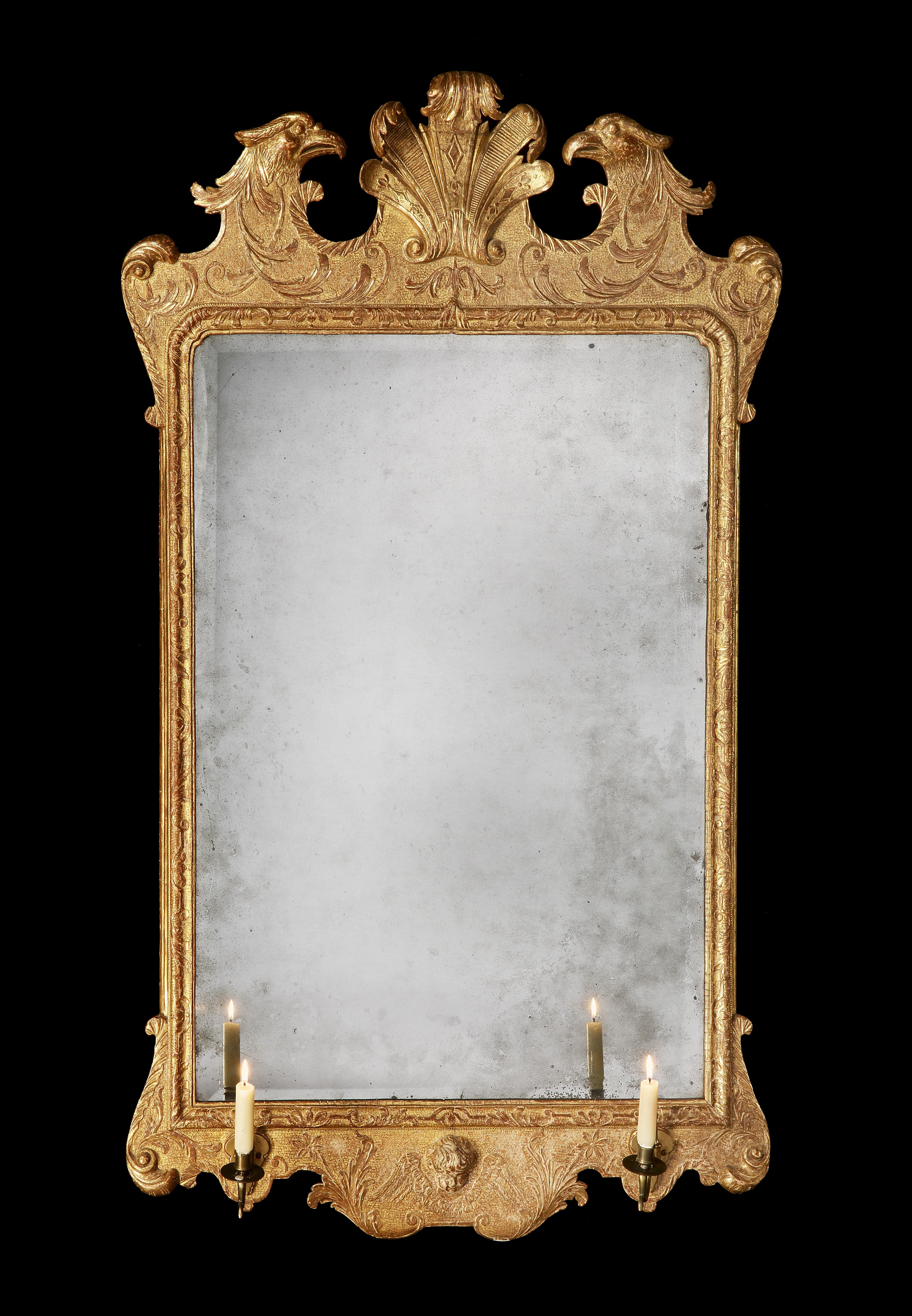 A very fine George II gilt gesso mirror. The rounded rectangular bevelled plate within a foliate-carved moulded frame, the cresting centred by feathers and flanked by eagles' heads on a pounced ground, the apron centred by a cherub mask and wings.
