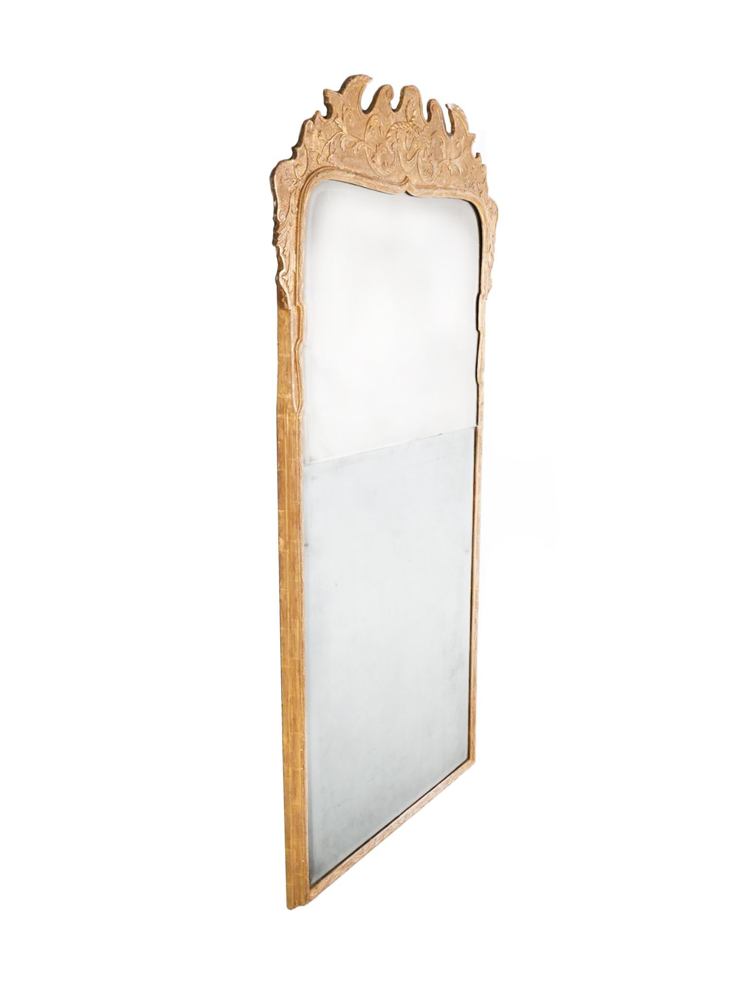 Handcrafted in the 18th Century, the frame of this tall George II wall mirror is made of giltwood and gesso. The front is decorated with carved vines and other ornate flourishes that culminate at the crest. The mirror itself consists of two beveled