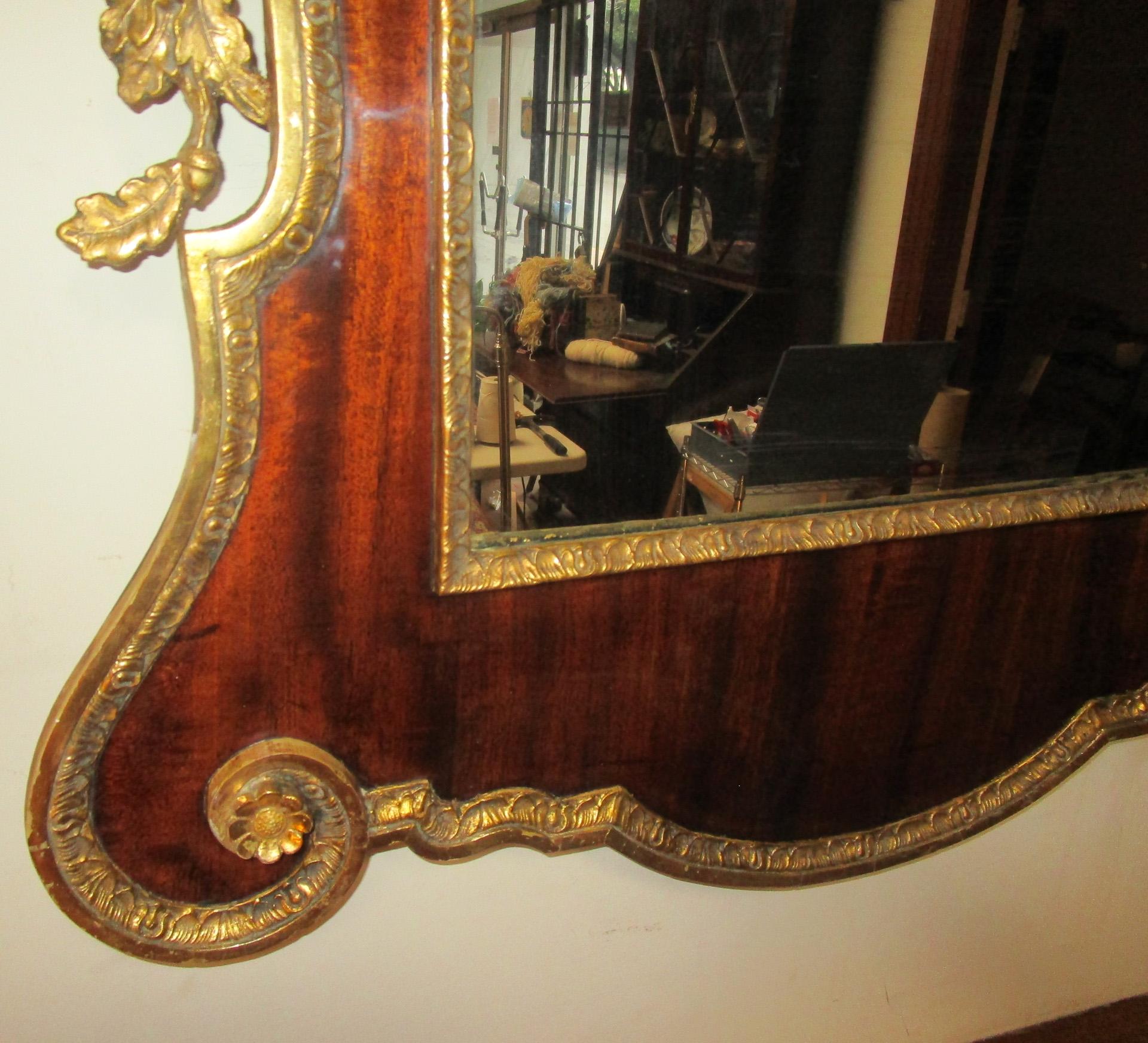 Handsome large size George II period English mirror of beautifully grained mahogany veneers with gilded embellishments. Features includes a broken pediment with center crest and intricate applied gilded foliate side decoration of acorns, oak leaf