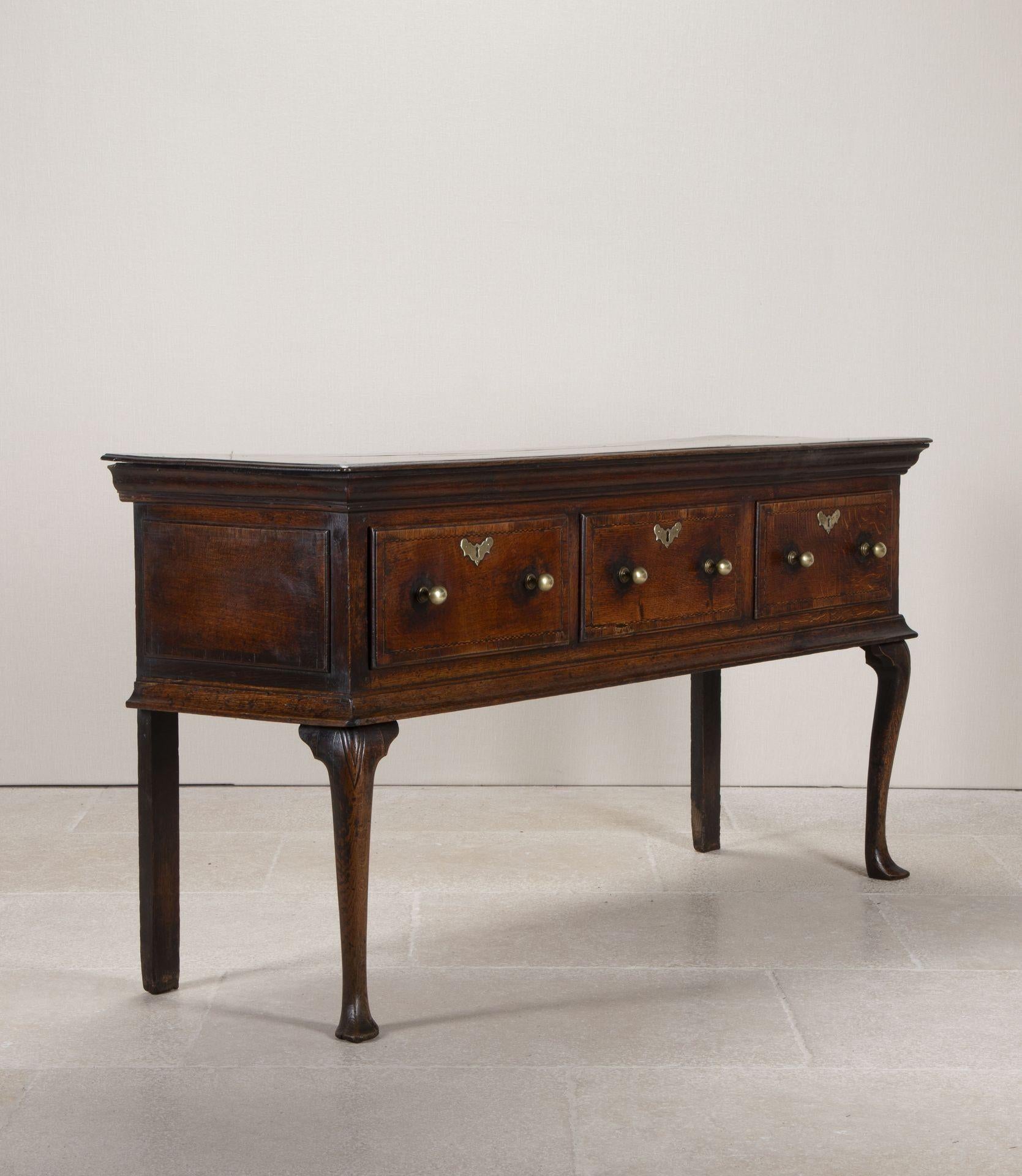 18th Century English George II period oak three drawer dresser base. Standing on two straight rear legs and two cabriole legs with carved detailing to the knees. With spade pad foot feet with a lovely rich deep patina with cast brass hardware the