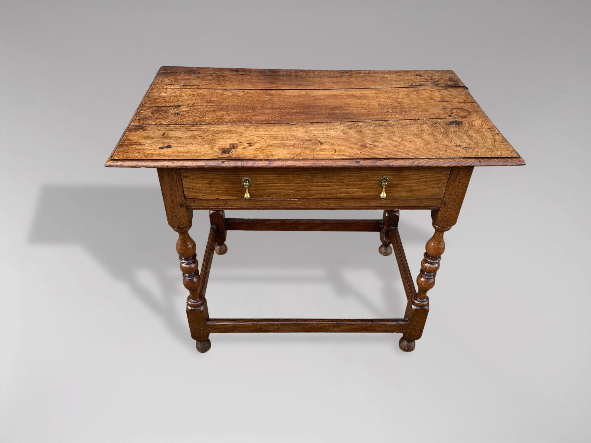 An early 18th century, George II period English solid oak lowboy. The rectangular three plank top with a thumbnail moulded edge above a single frieze long drawer with original brass teardrop handles, raised on four turned legs adjoined by