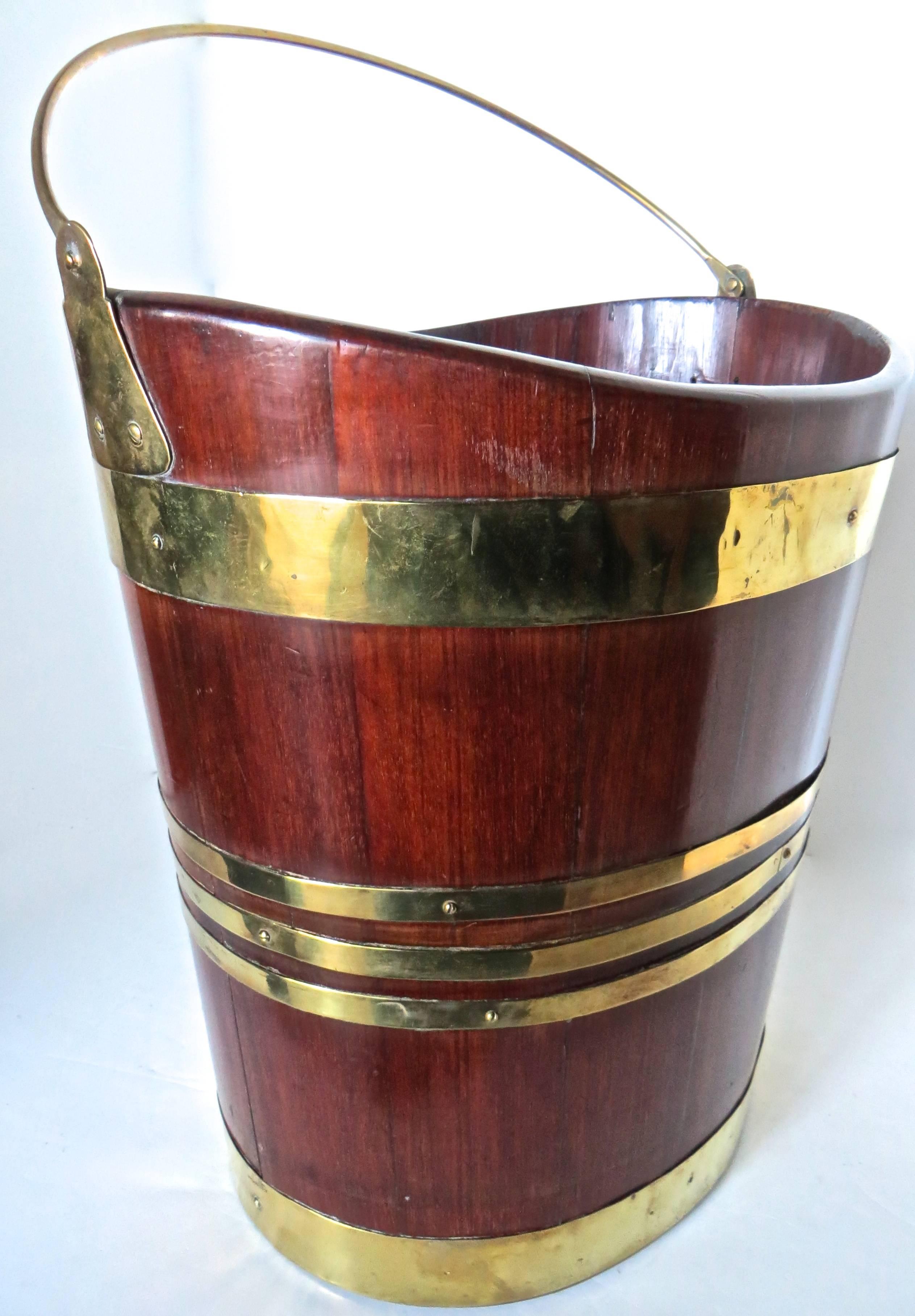This very attractive British made oval shaped and tapered mahogany peat bucket is elaborately decorated and bound with five brass bands, and is held at the top with the original brass bale, held in place by the original side brass mounts, circa