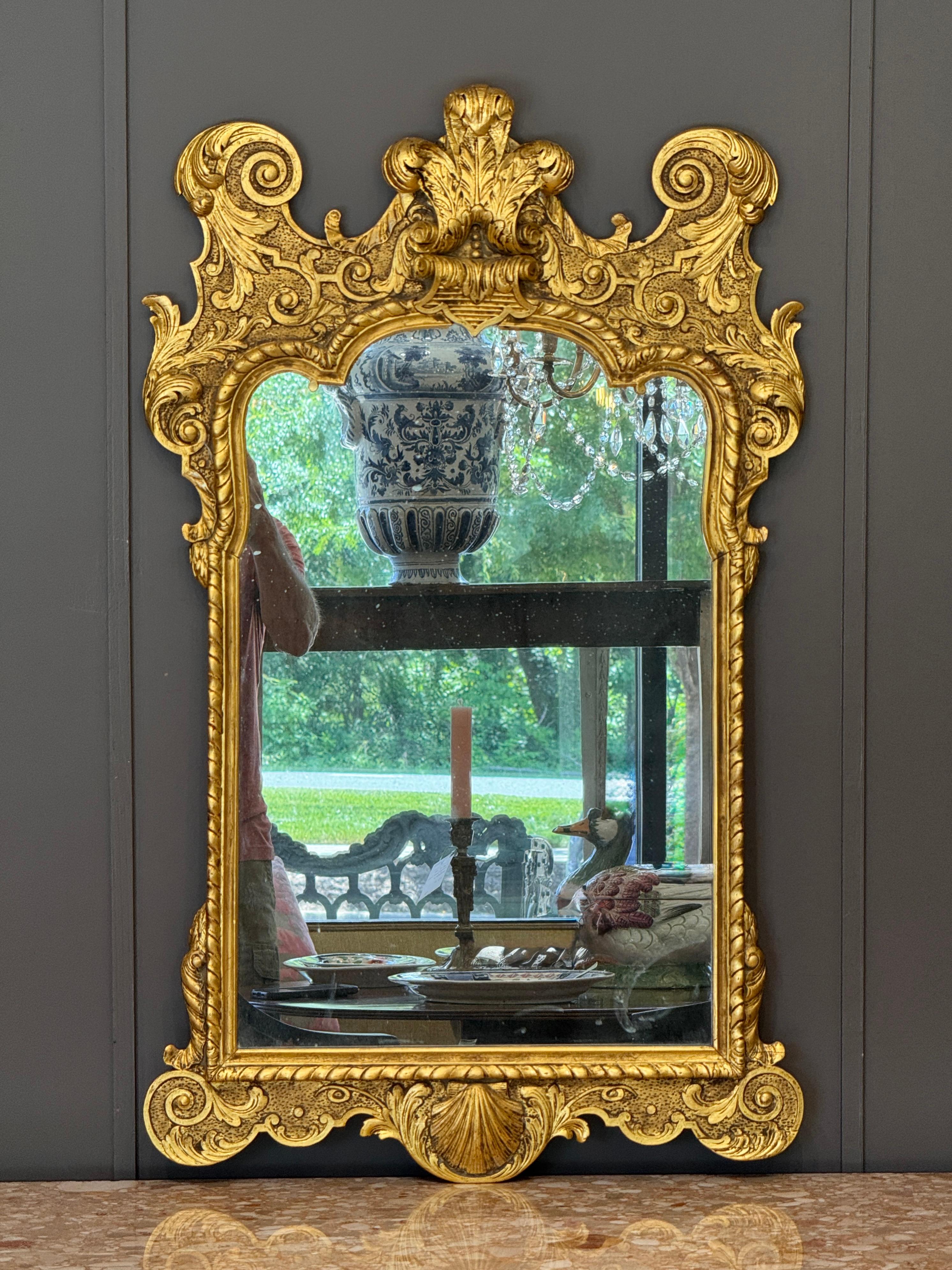 Englischer Vergoldungsspiegel aus dem 18. Jh. mit geschnitztem Rokoko-Rollwerk und Akanthusblatt-Ornamenten. Das Wappen weist reichhaltige Details in Form von Federn und Voluten auf. Die ursprüngliche vergoldete Oberfläche weist eine attraktive