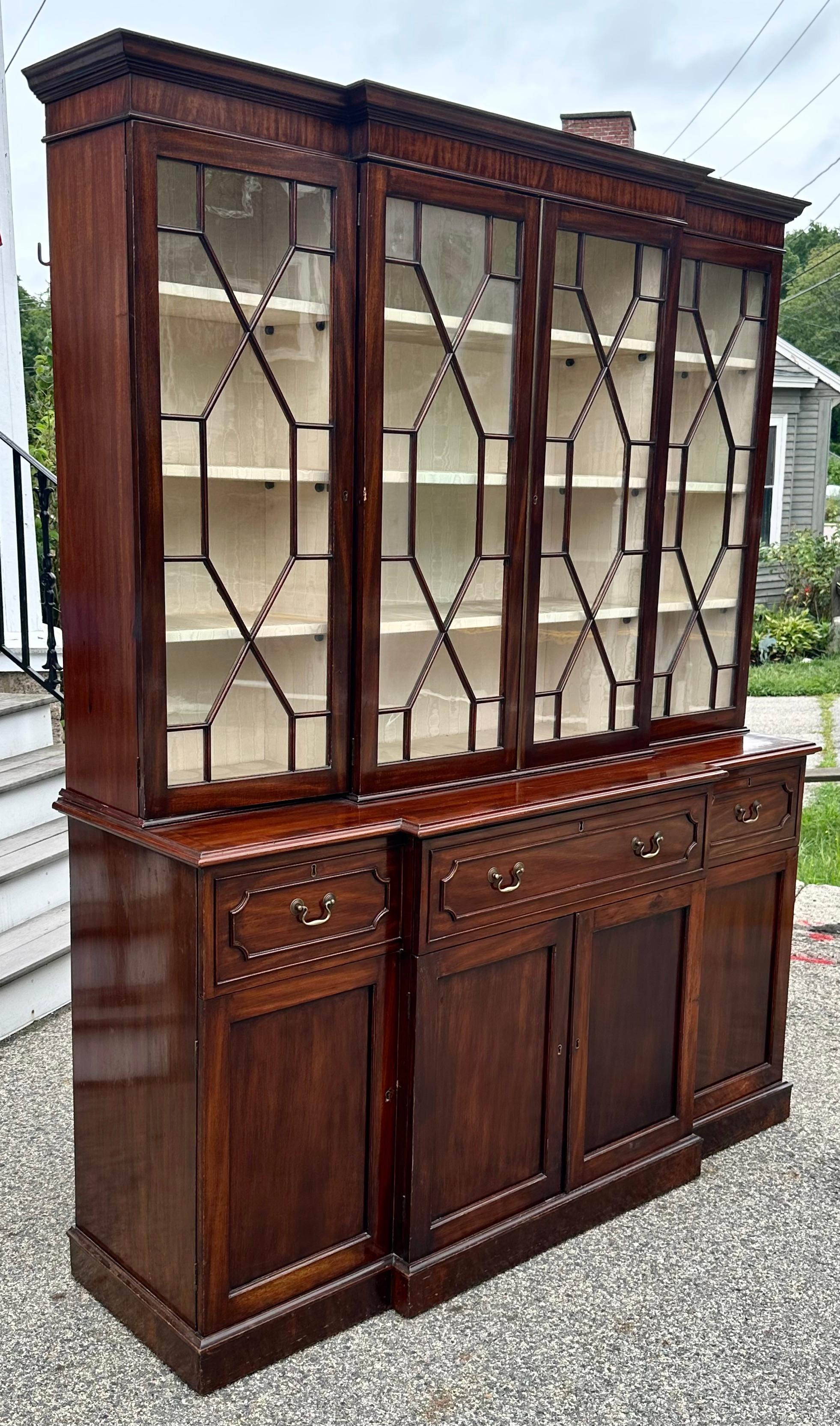 George III Period Mahogany Breakfront, Late 18th Century.  Beautifully fenestrated upper case with original glass.  Silk moire covered, adjustable shelves.  Cabinet base with desk in middle drawer showcasing a magnificent cubbyholed interior of