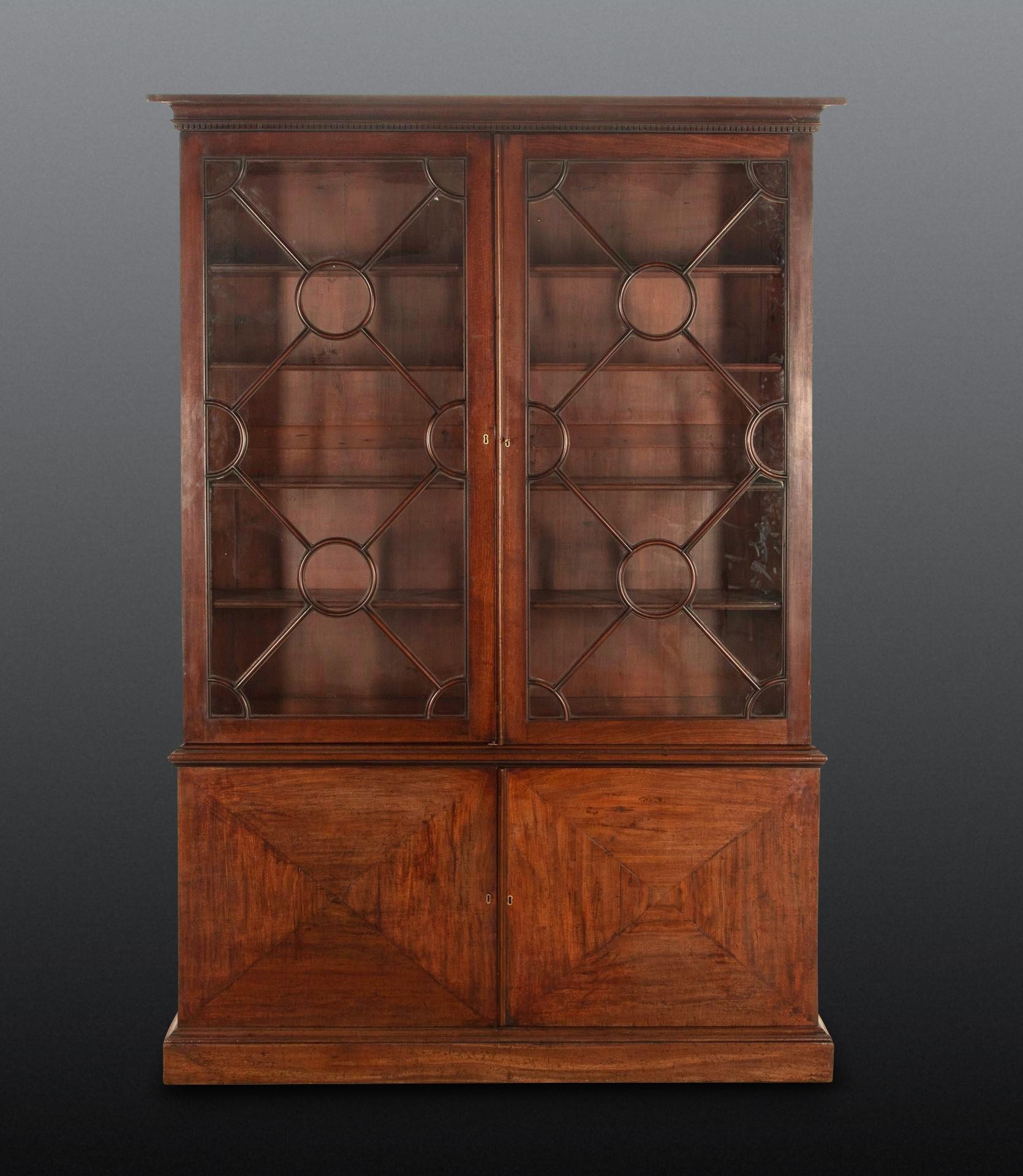 Impresionante librería de caoba del siglo XVIII, posiblemente de Henry Hill of Marlborough, con cornisa cóncava y molduras dentiladas sobre un par de inusuales puertas acristaladas circulares y romboidales con moldura escalonada en la cintura y un