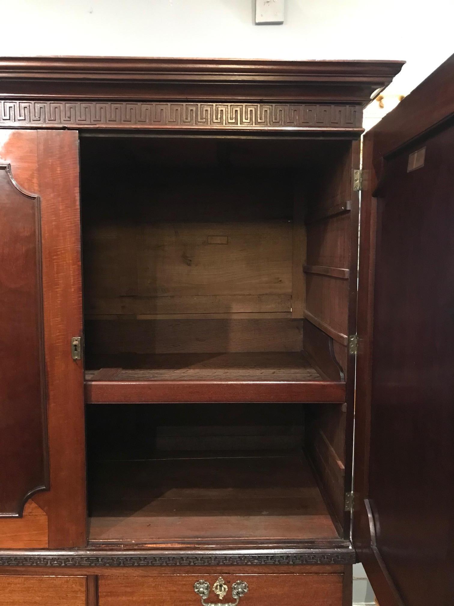 18th century George III mahogany linen cupboard in the manner of Chippendale, the moulded and stepped cornice raised over frieze with carved Greek key blind fretwork opening to reveal concealed drawer above two book matched doors with shaped and