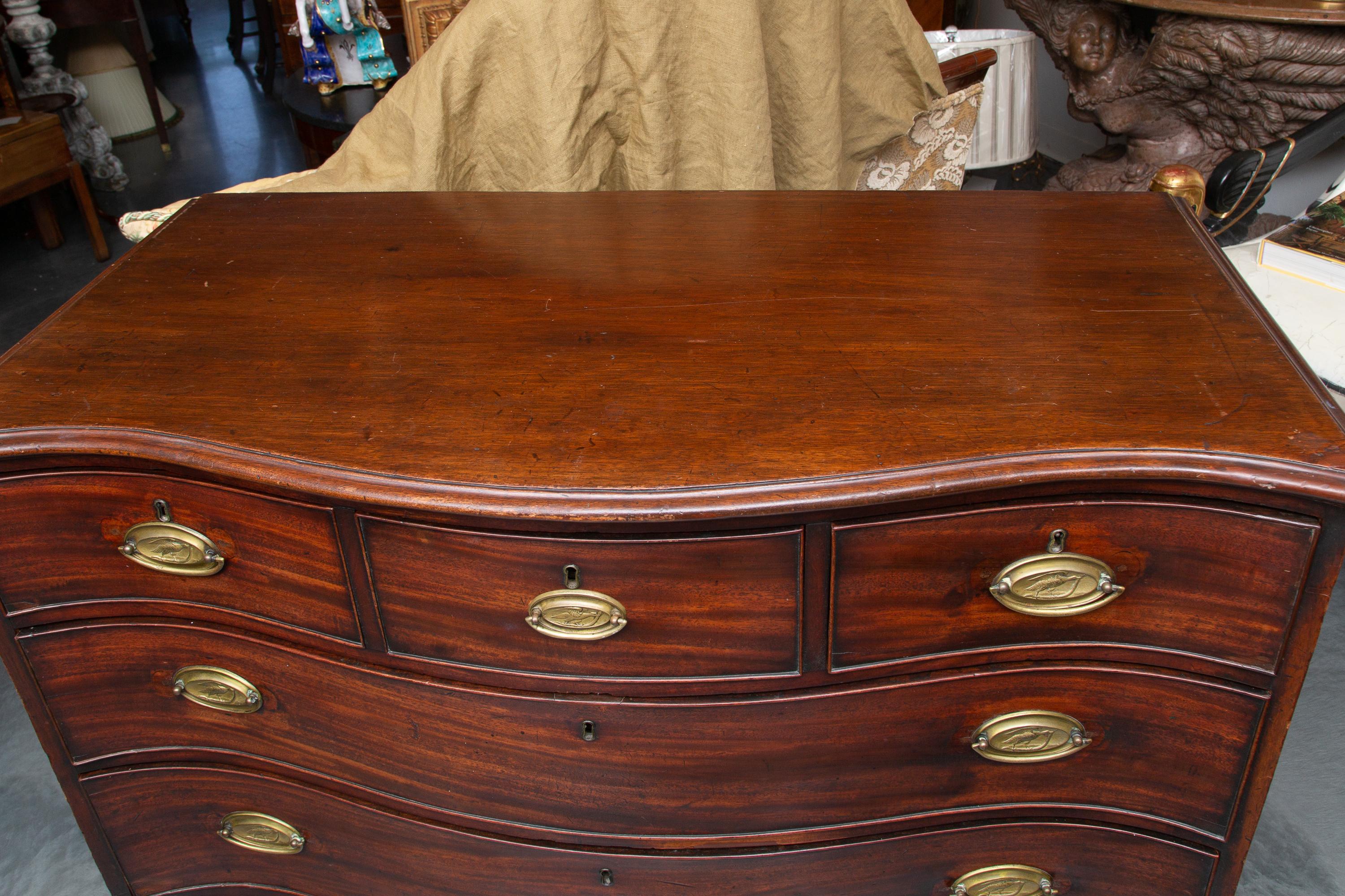 This is a classic late 18th century English George III solid mahogany serpentine chest of drawers. This lovely, mellow chest has a top with a molded edge, over three short and three long, graduated drawers. The chest of drawers is situated on shaped